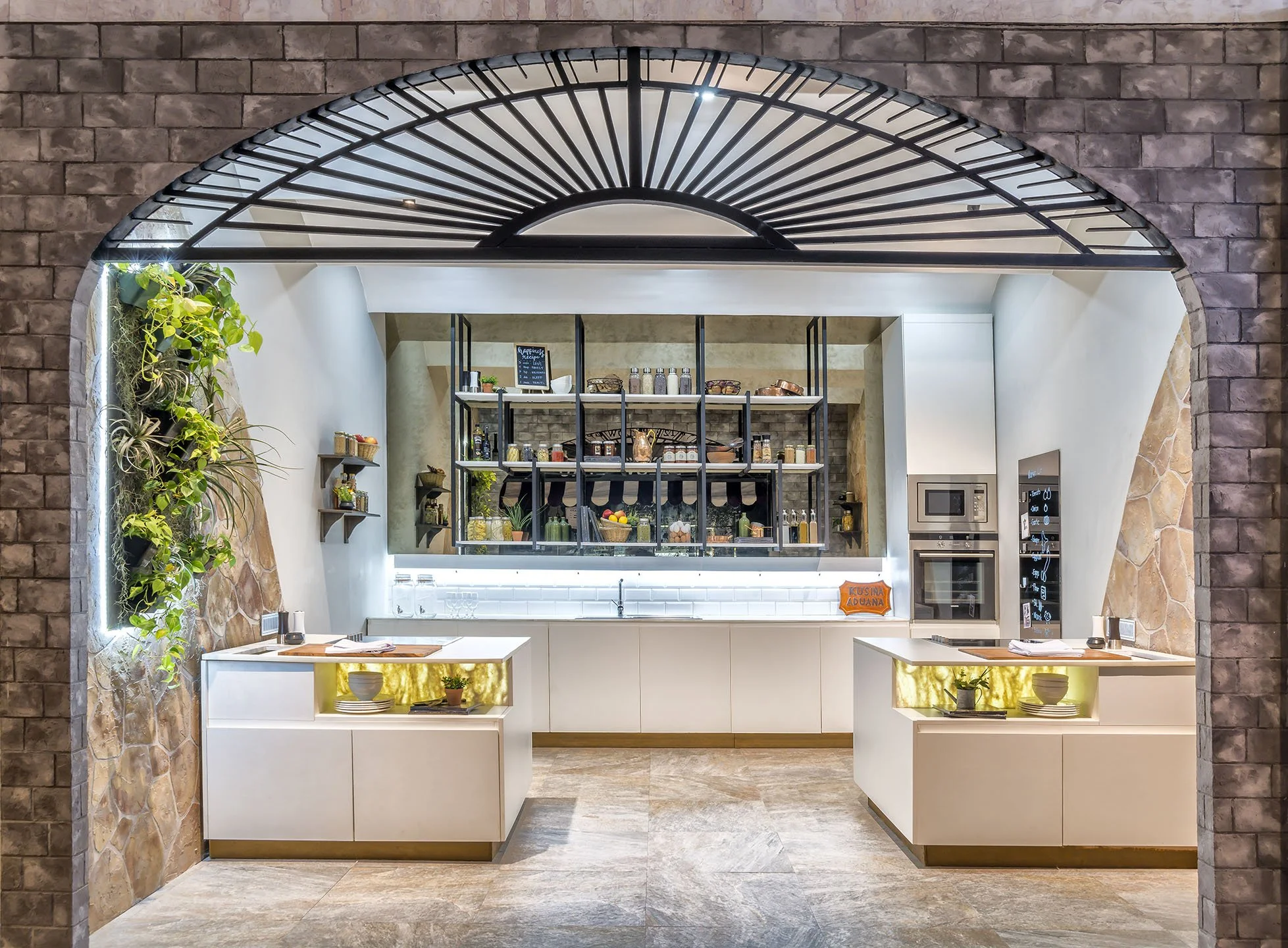 A view of a modern cafe with brick walls and a decorative black metal arch framing the entrance, showing an interior with shelves of products, a chalkboard menu, and white countertops with gold accents.