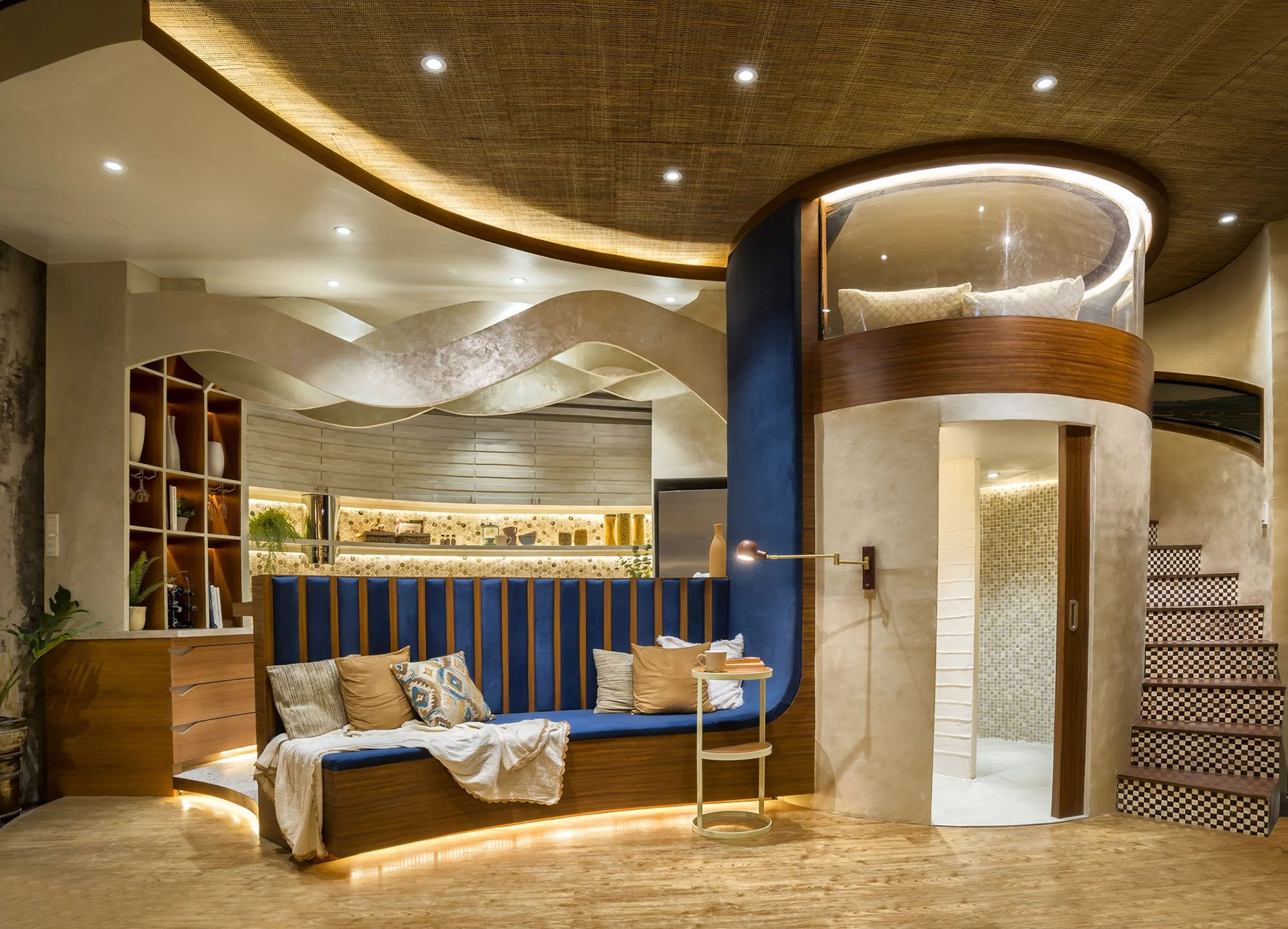 Interior view of a modern living space with a cozy built-in sofa with pillows, a small side table, decorative wall features, and a ceiling with recessed lighting, crafted with natural materials and warm lighting.
