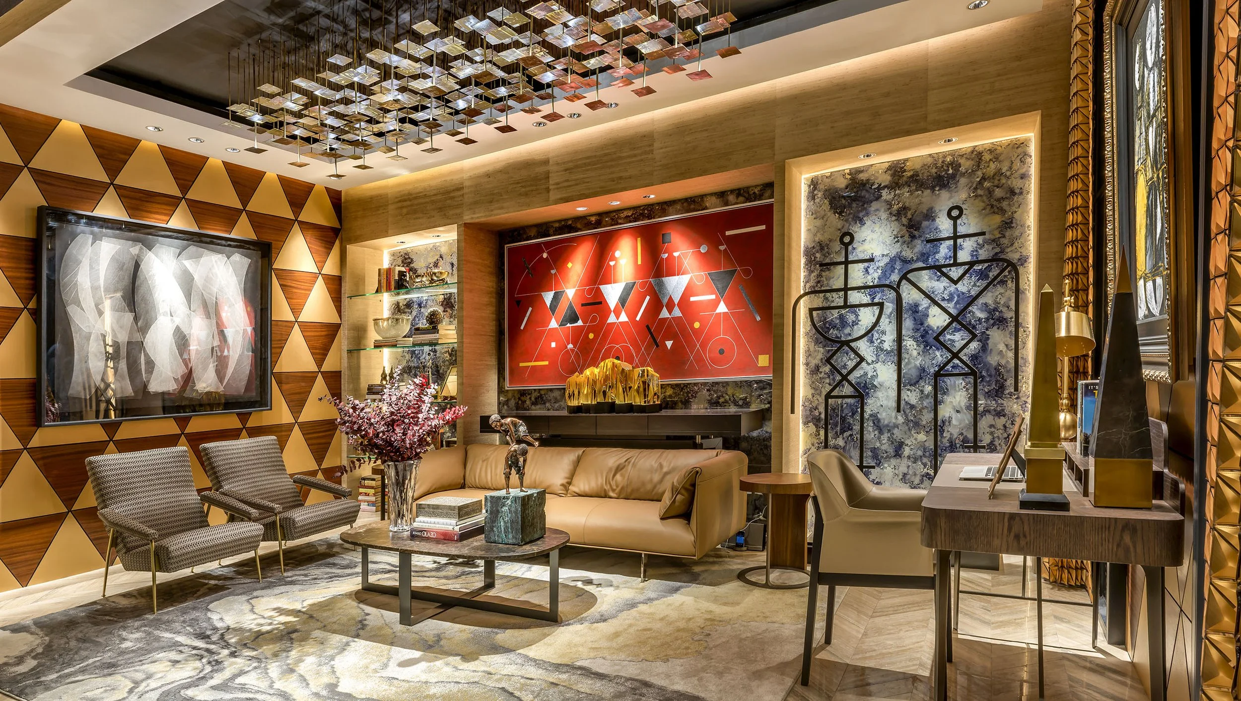 A modern living room with decorative art on the walls, including a red abstract painting and a blue textured piece with black line art. The room features warm wood paneling, a geometric wall design, and a decorative ceiling sculpture. The space includes a beige sofa, patterned chairs, a glass-topped coffee table, and various ornaments and books, creating a stylish and inviting atmosphere.