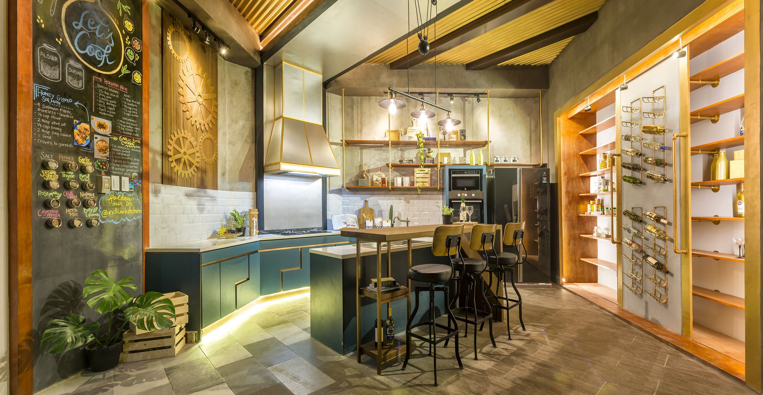 Modern kitchen with a teal island, black chairs, decorative wall gears, a chalkboard menu, and open shelving with various kitchen items in a warm, stylish setting.