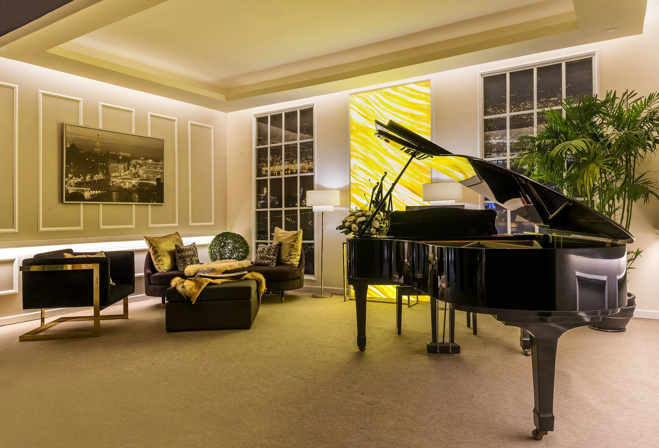 Living room with grand piano, a sofa with pillows, a large picture of a city skyline on the wall, a floor lamp, a large plant by windows, and a yellow abstract art piece behind the piano.