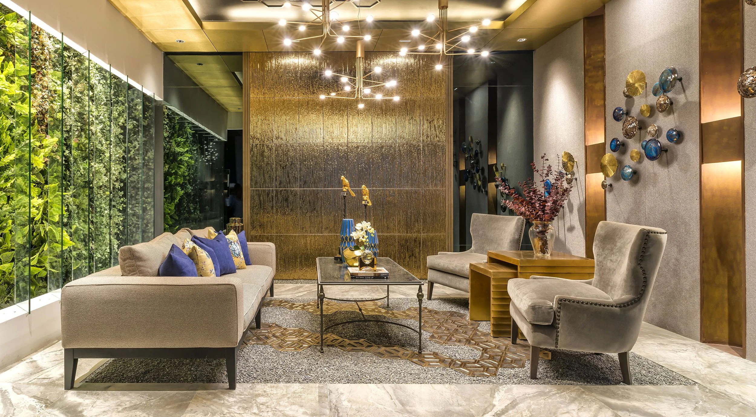 Interior of a modern hotel lobby or lounge with beige and gray furniture, decorative wall art, a gold-textured wall, a green living wall, and contemporary lighting fixtures.