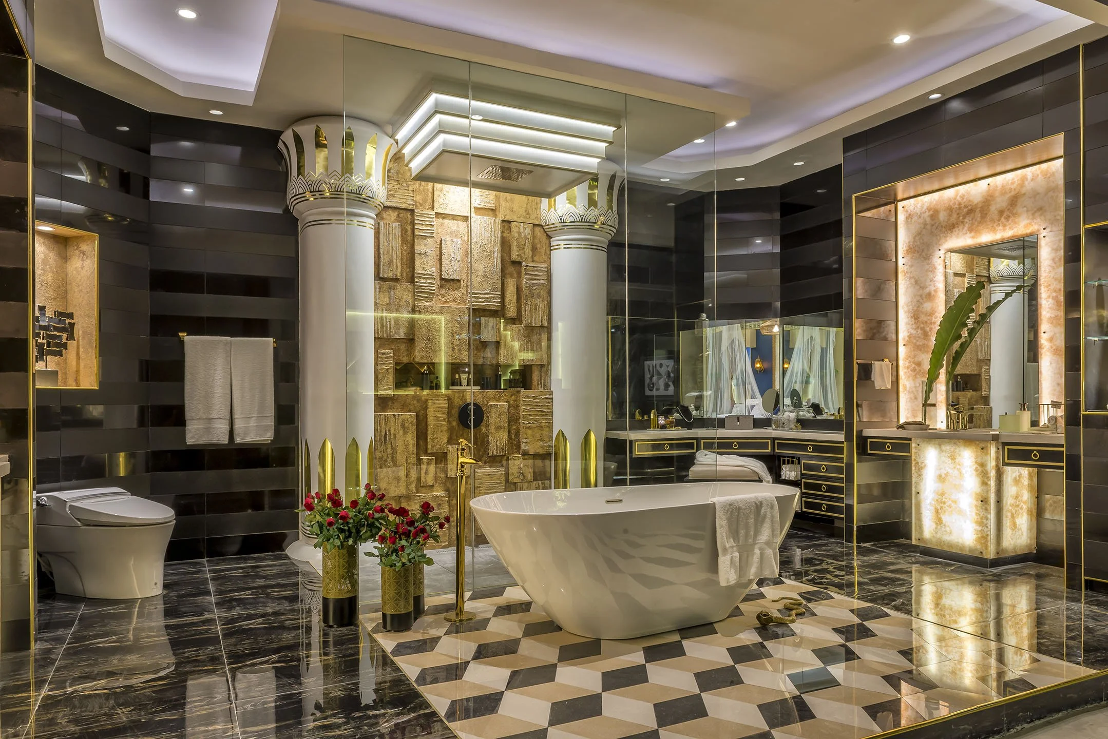 Luxurious bathroom with black and gold accents, featuring a freestanding bathtub, a separate shower with glass walls, a gold-trimmed mirror, a toilet, and elegant decor including red flowers, green plants, and textured wall panels.