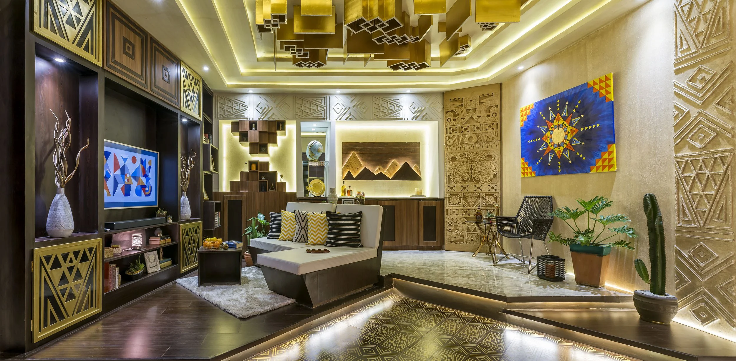 Modern living room with geometric and tribal patterned decor, wooden shelving with books and vases, a white sofa with striped and zigzag pillows, colorful artwork on the walls, potted plants, and warm recessed lighting.