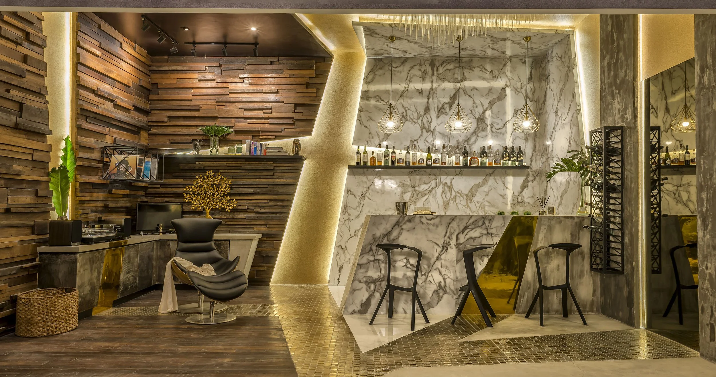 Modern interior of a bar or lounge with wood-paneled and marble walls, bar counter with various liquor bottles, pendant lighting, and seating area with black chairs and decorative plants.