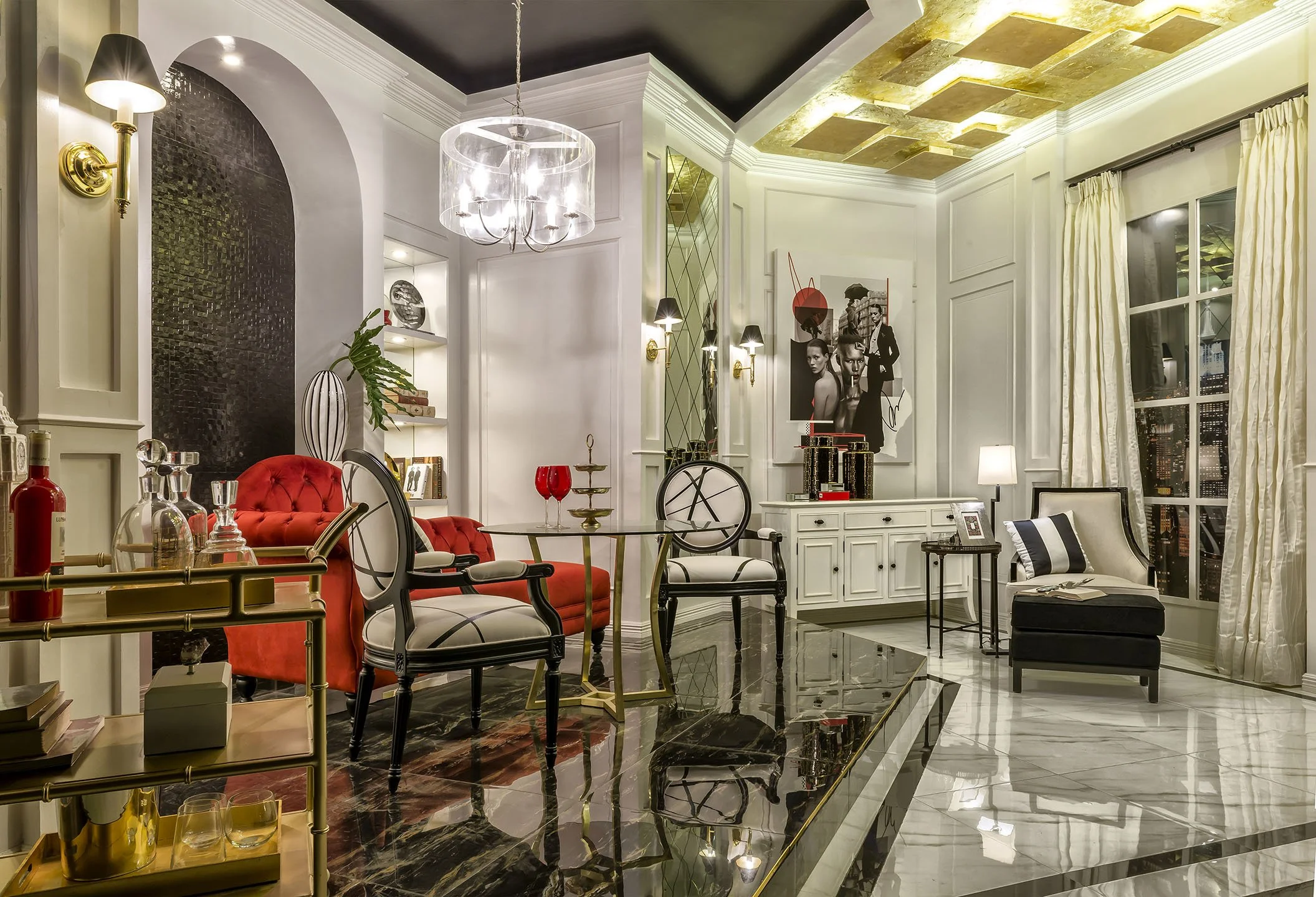 A luxurious living room with white walls, and gold accents on the ceiling and furniture. There are black, white, and red chairs, a glass chandelier, and a large window with cream curtains. Decor includes artwork, a plant, and decorative objects on shelves, with a shiny marble floor.
