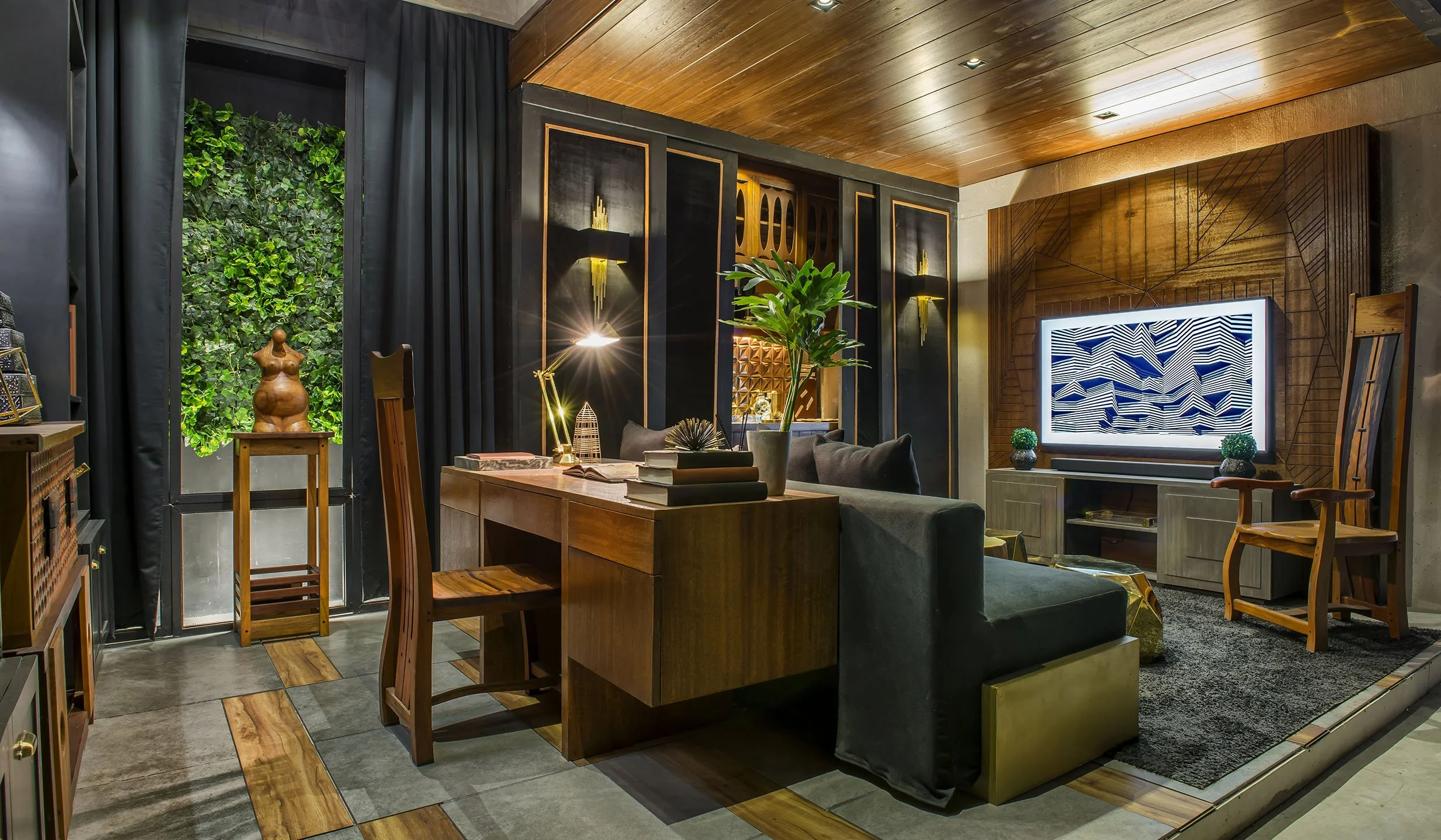 Interior of a modern living room with wood-paneled ceiling, black and wooden wall panels, a large flat-screen TV with abstract black and white art, a green sofa, a wooden table with books and decorative items, a potted plant, and a large window with black curtains showing greenery outside.