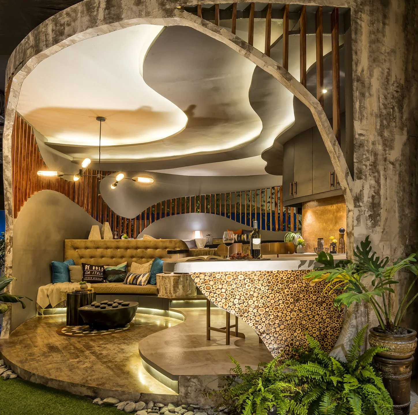 Interior of a modern, artistically designed living space with flowing, sculptural ceiling, cozy seating area with cushions, and a bar countertop made of unique patterned wood. Green plants add a natural touch to the space.