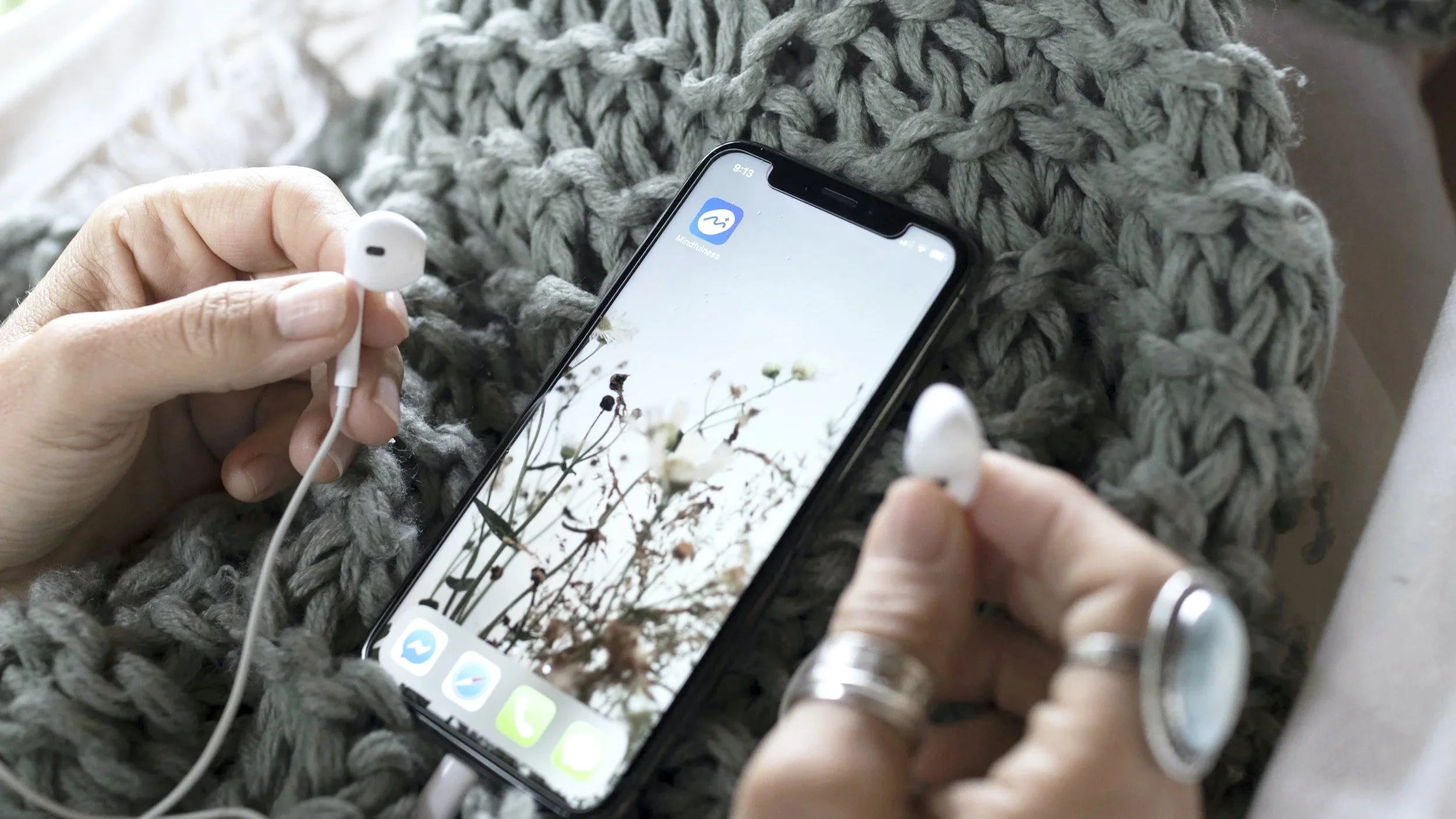 Person holding earphones about to listen to a mindfulness app on their phone.