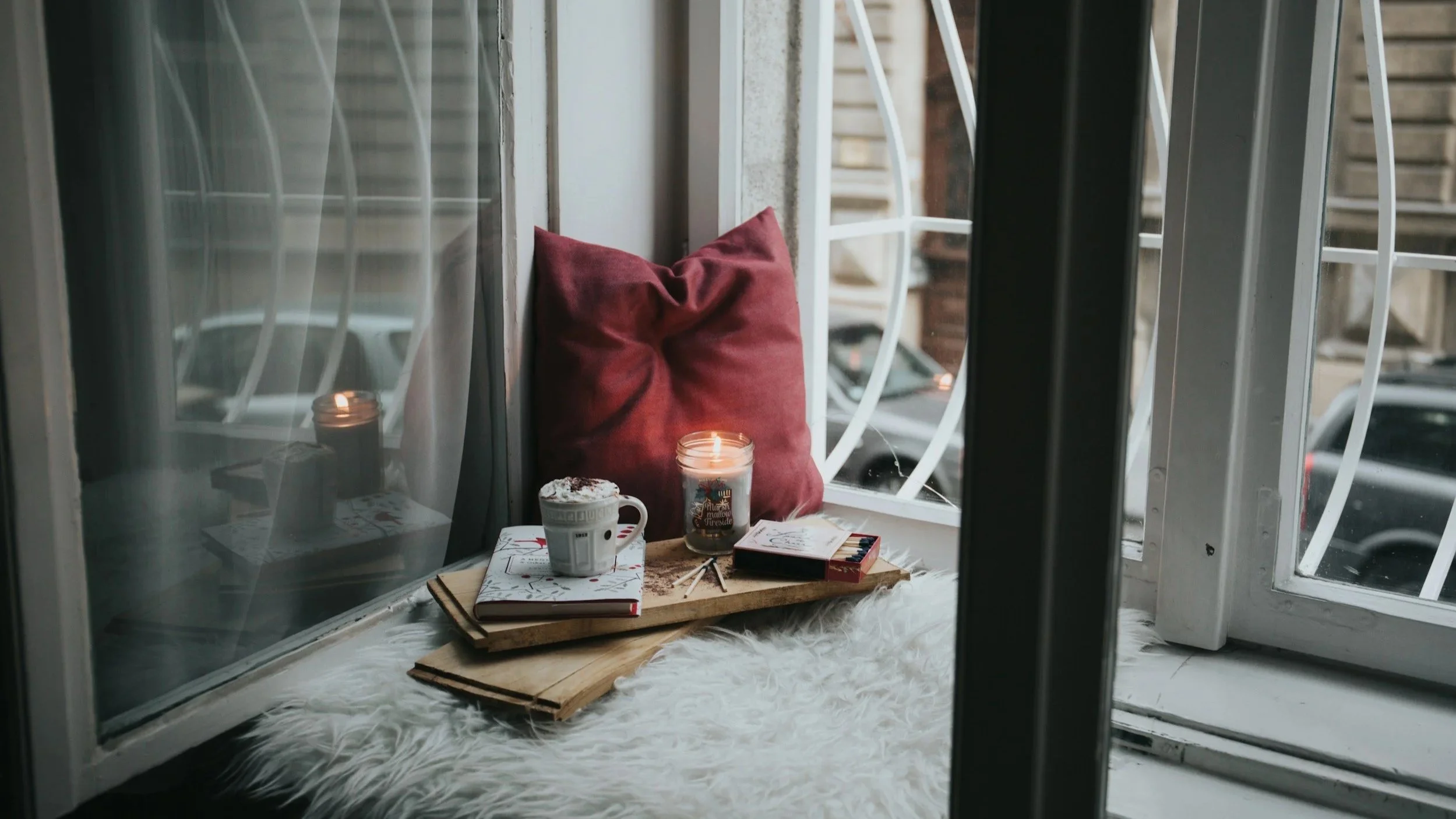 Window seat with pillow, books, a lit candle and a cup of something hot symbolising calm resolution of boundaries.