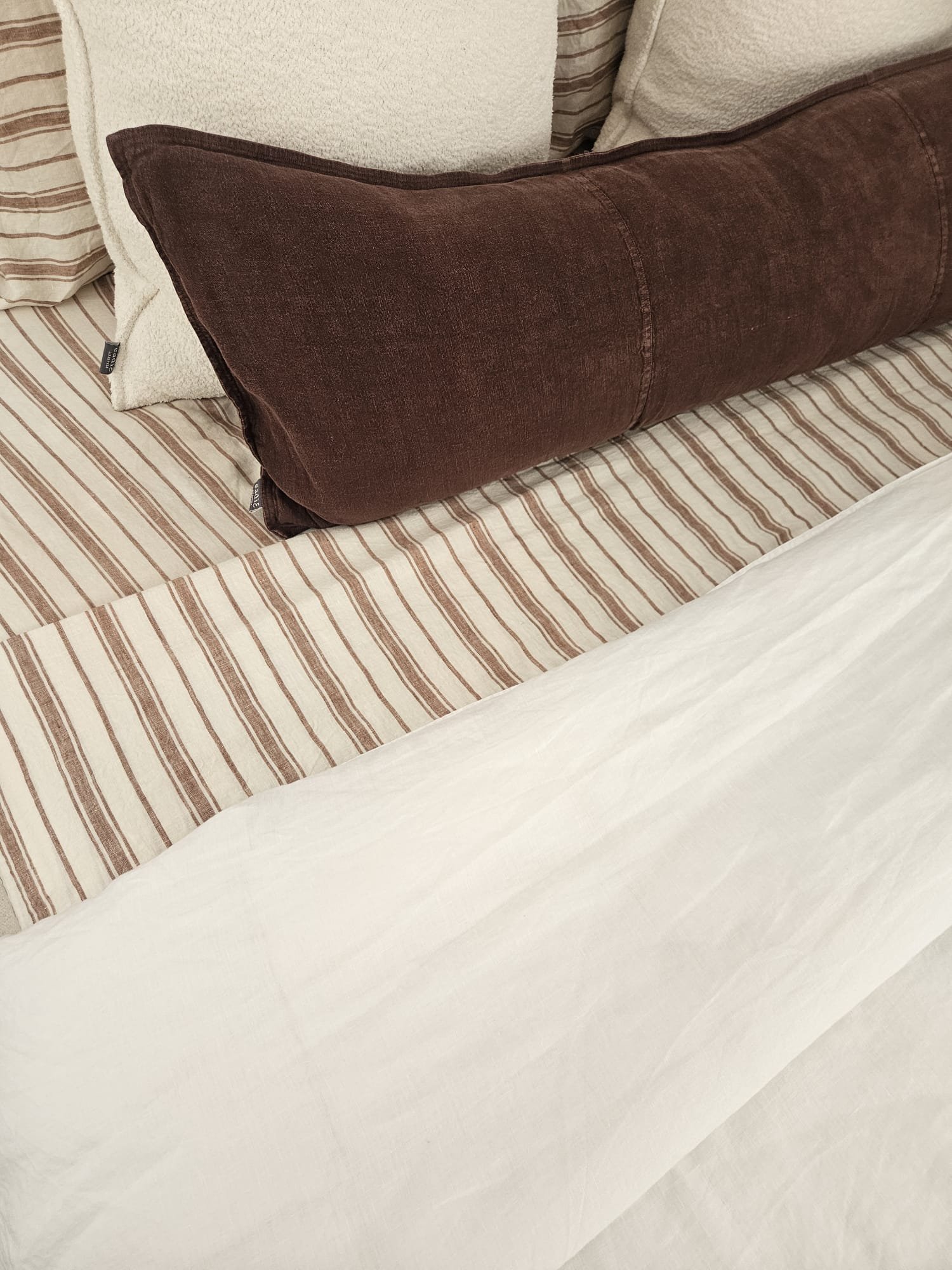 Brown velvet bolster cushion on striped linen bedding, Glenelg Retreat, Young & Co Interiors