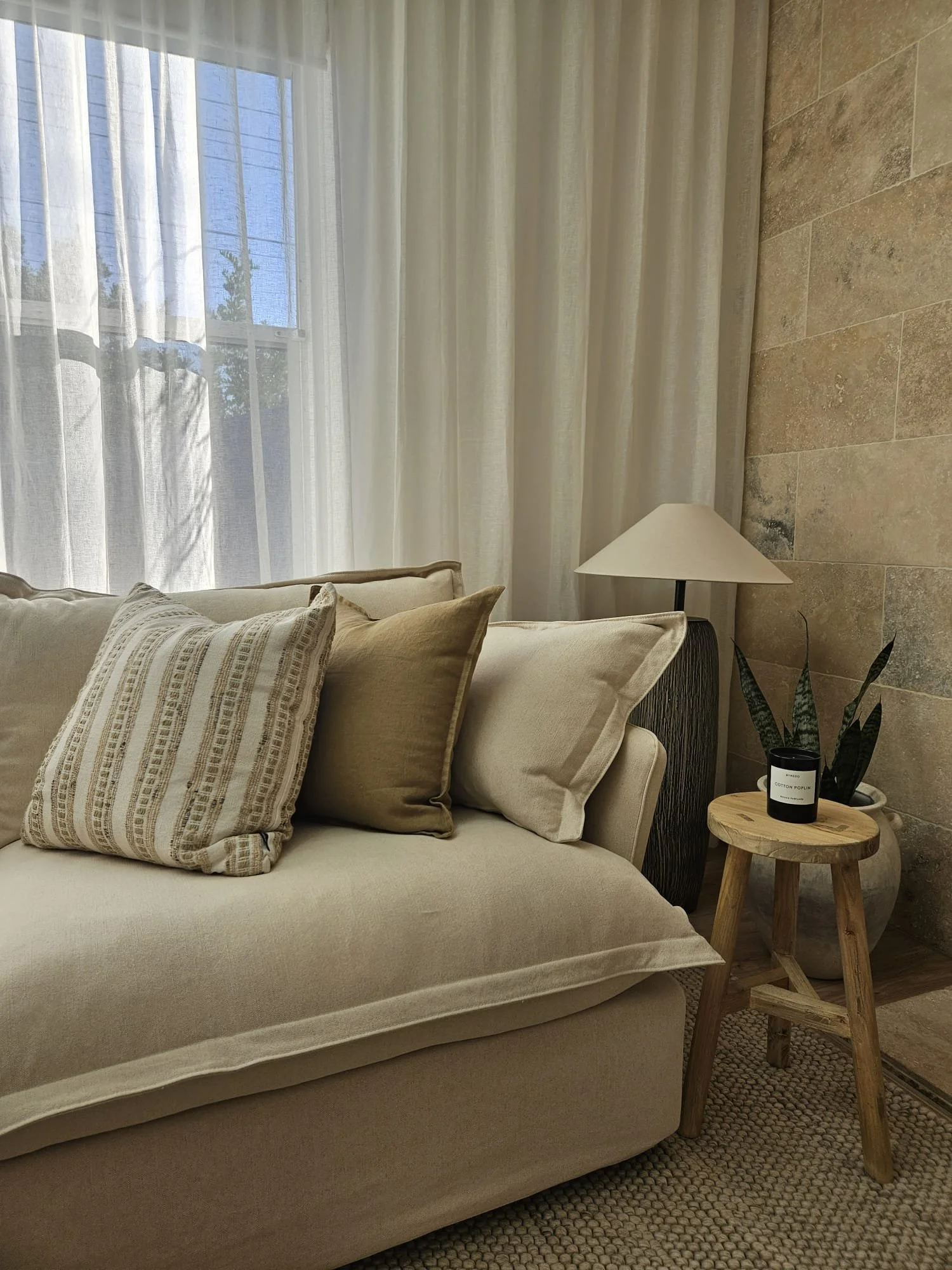 Linen sofa with textured cushions and ceramic lamp beside a travertine stone feature wall, Glenelg Retreat living room by Young & Co Interiors