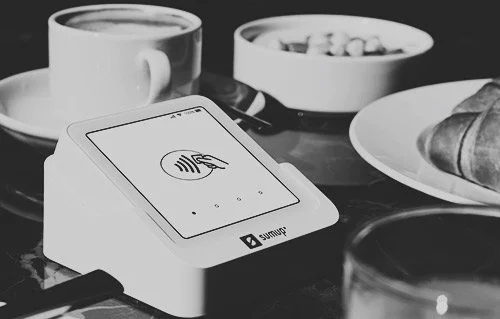 A modern payment terminal next to a cup of coffee on a table, monochrome.