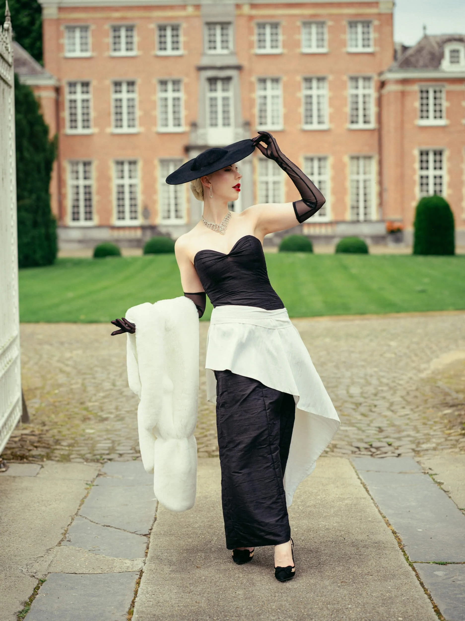 Yulia wearing a black hat and red dress standing at the gate of Château Belvedère