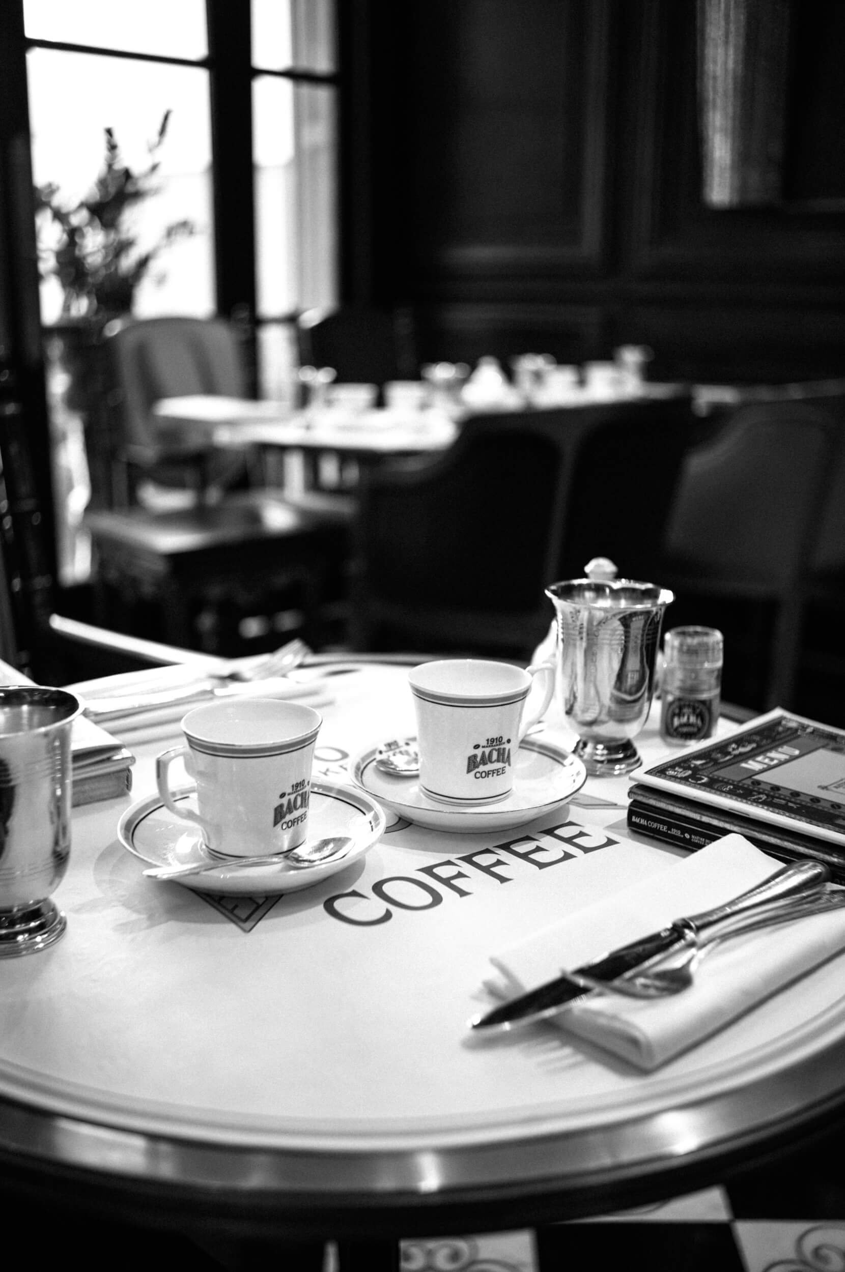 Black and white photograph of coffee cups and tableware at Bacha Coffee on the Champs-Élysées in Paris.