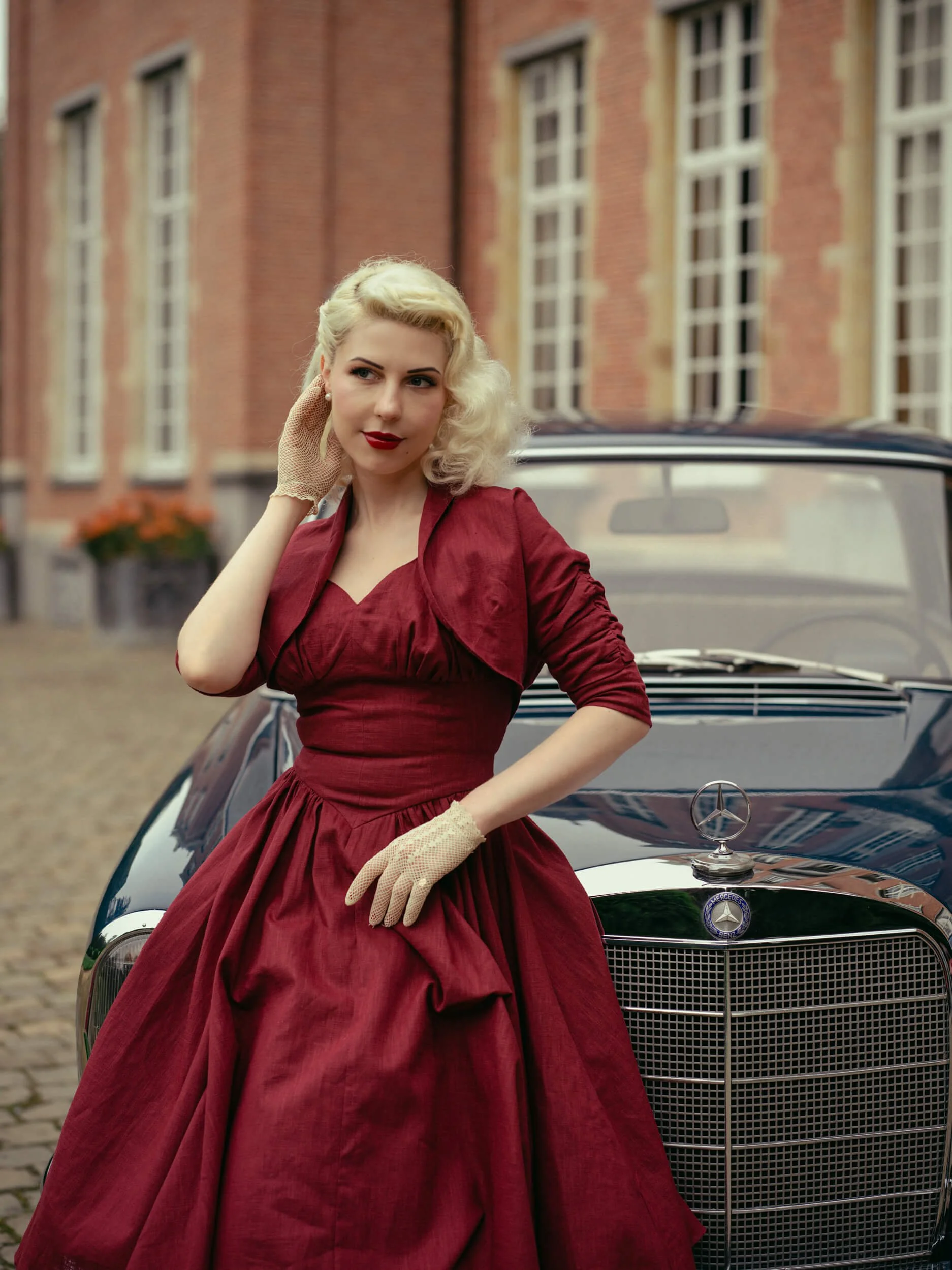 Yulia in a red dress standing beside a vintage Mercedes-Benz 220