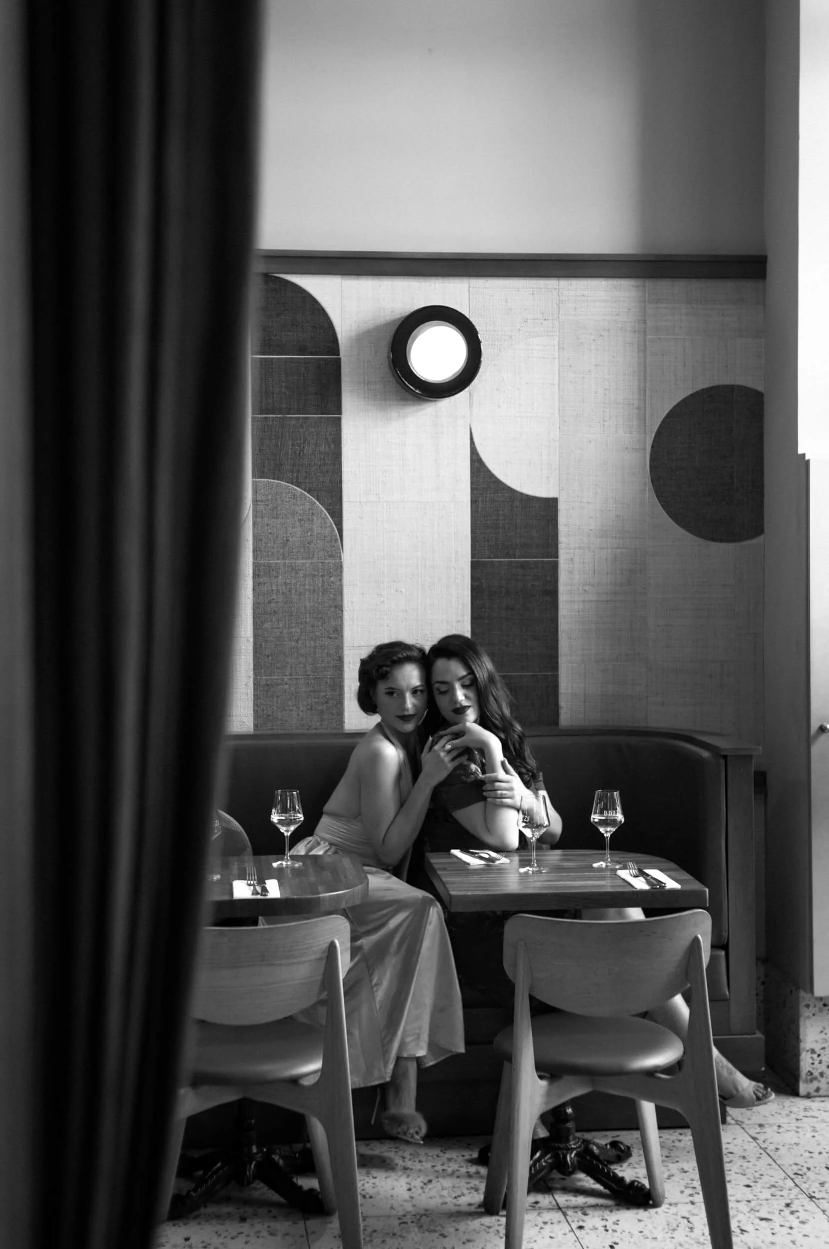 Black and white photograph of two women sitting together in a restaurant interior photographed with the Omnar Bertele 50mm f/2