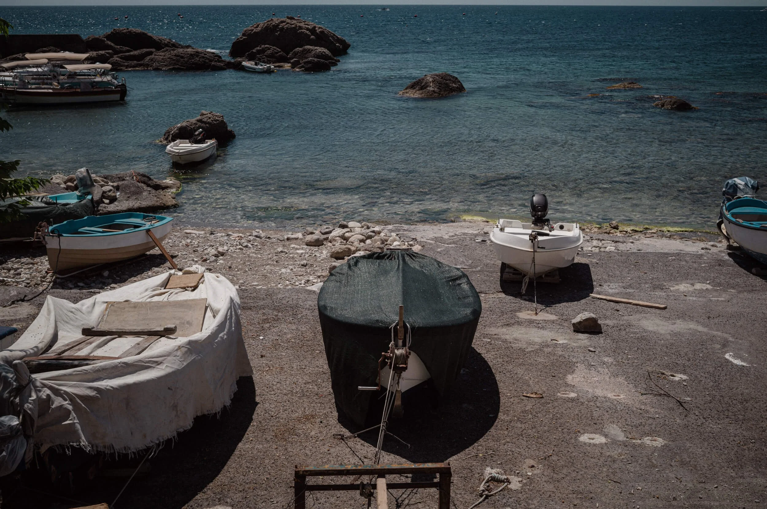 Small fishing boats resting beside a rocky shoreline on the Sicilian coast photographed with the Thypoch Ksana 35mm f/2
