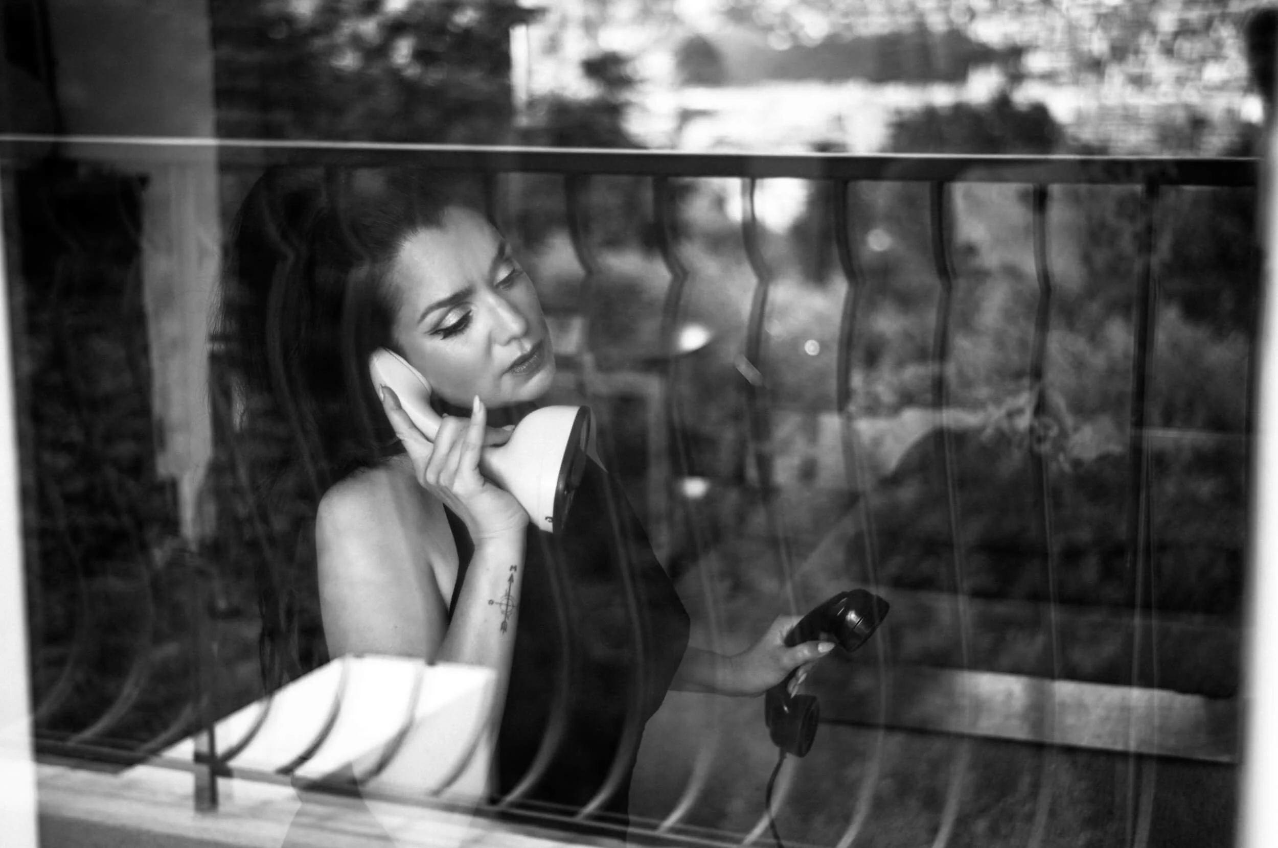 Flo holding a vintage telephone behind a reflective window in Nice photographed with the Omnar Bertele 50mm f/2 on the Leica M11 Monochrom
