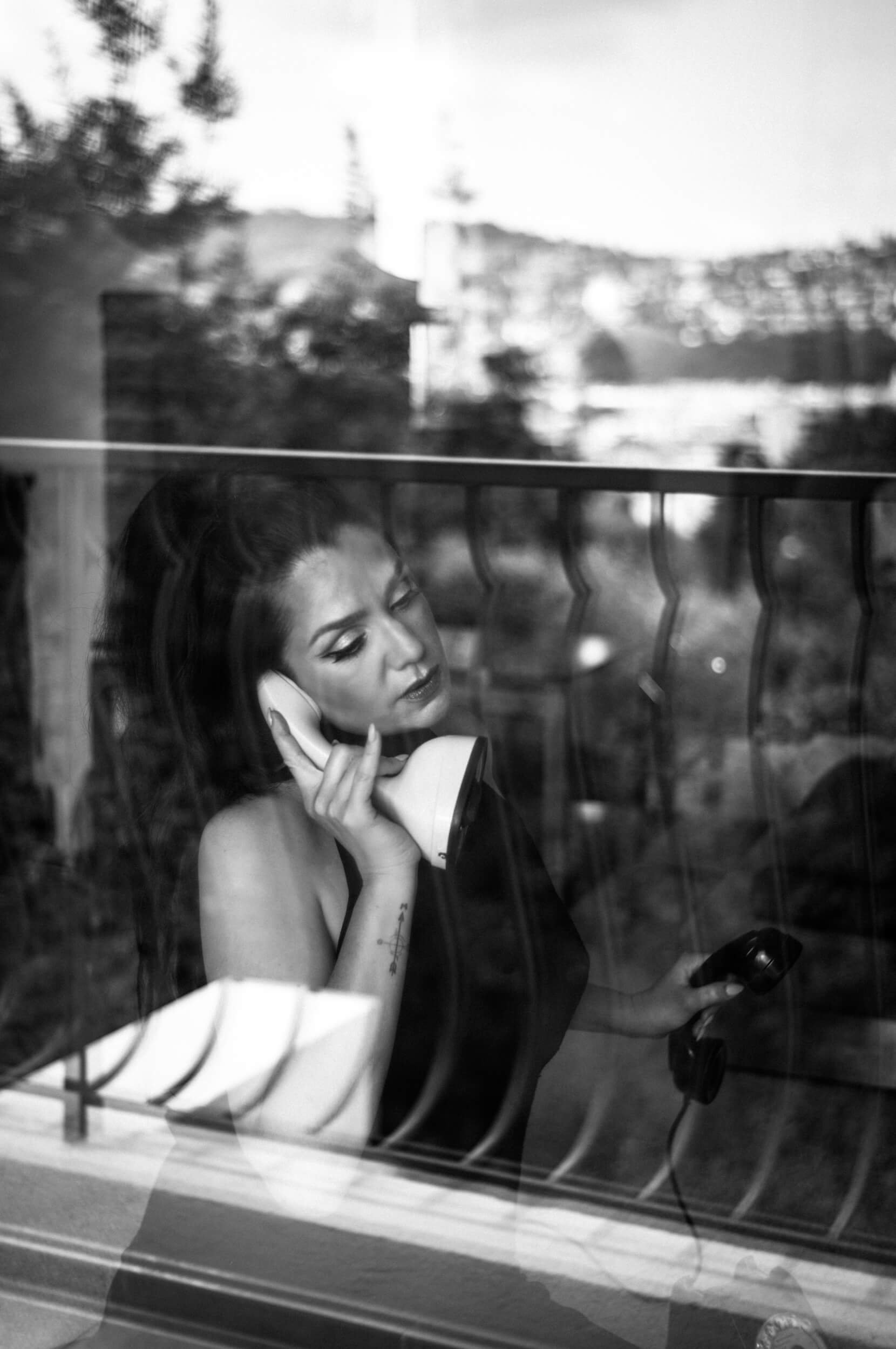 Black and white portrait through a window reflection of a woman holding a vintage telephone photographed with the Omnar Bertele 50mm f/2