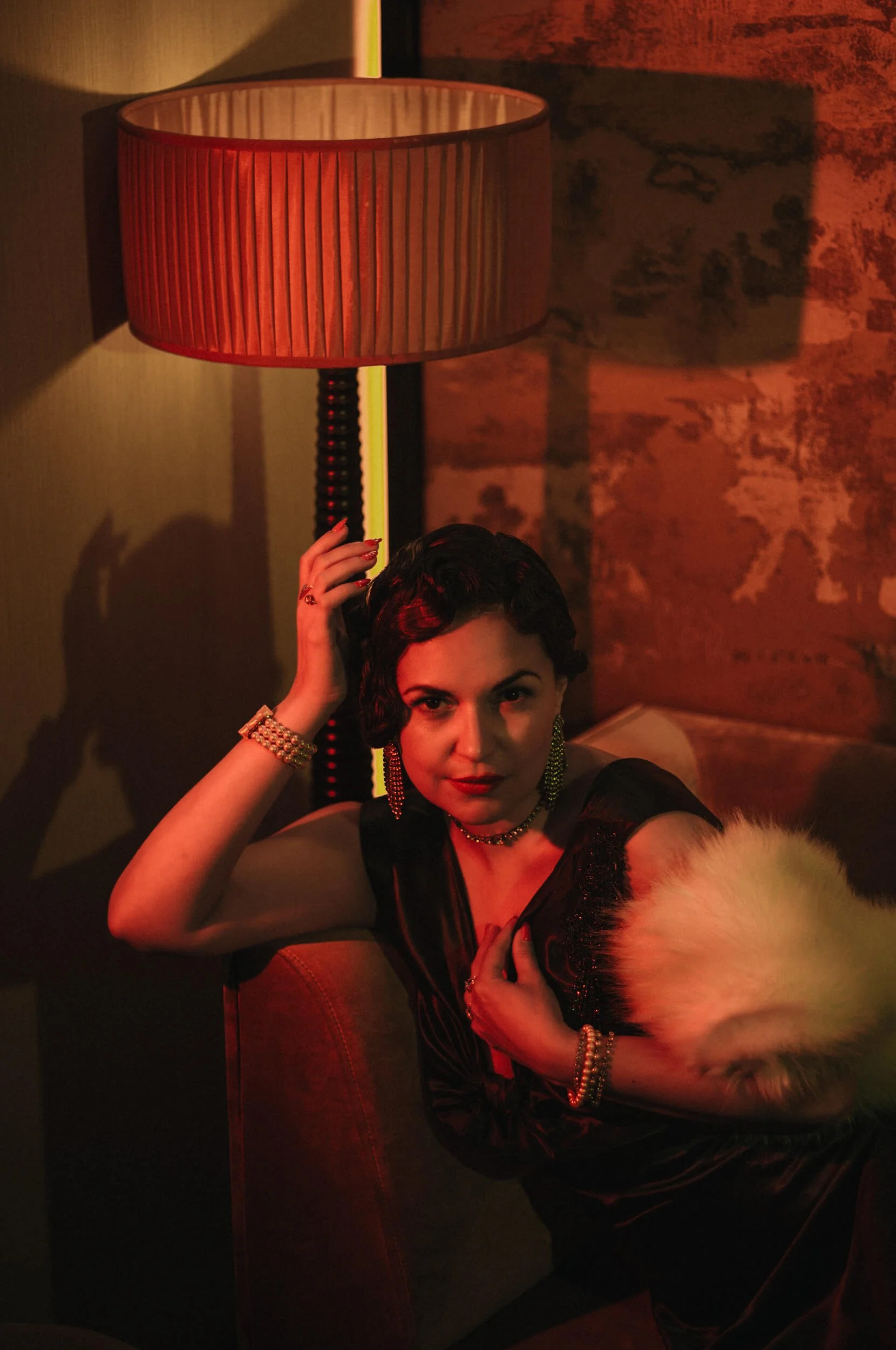 Aude reclining on a sofa at Minuit Express cocktail bar in Hôtel La Bourdonnais, Paris, photographed with warm red and amber lighting.