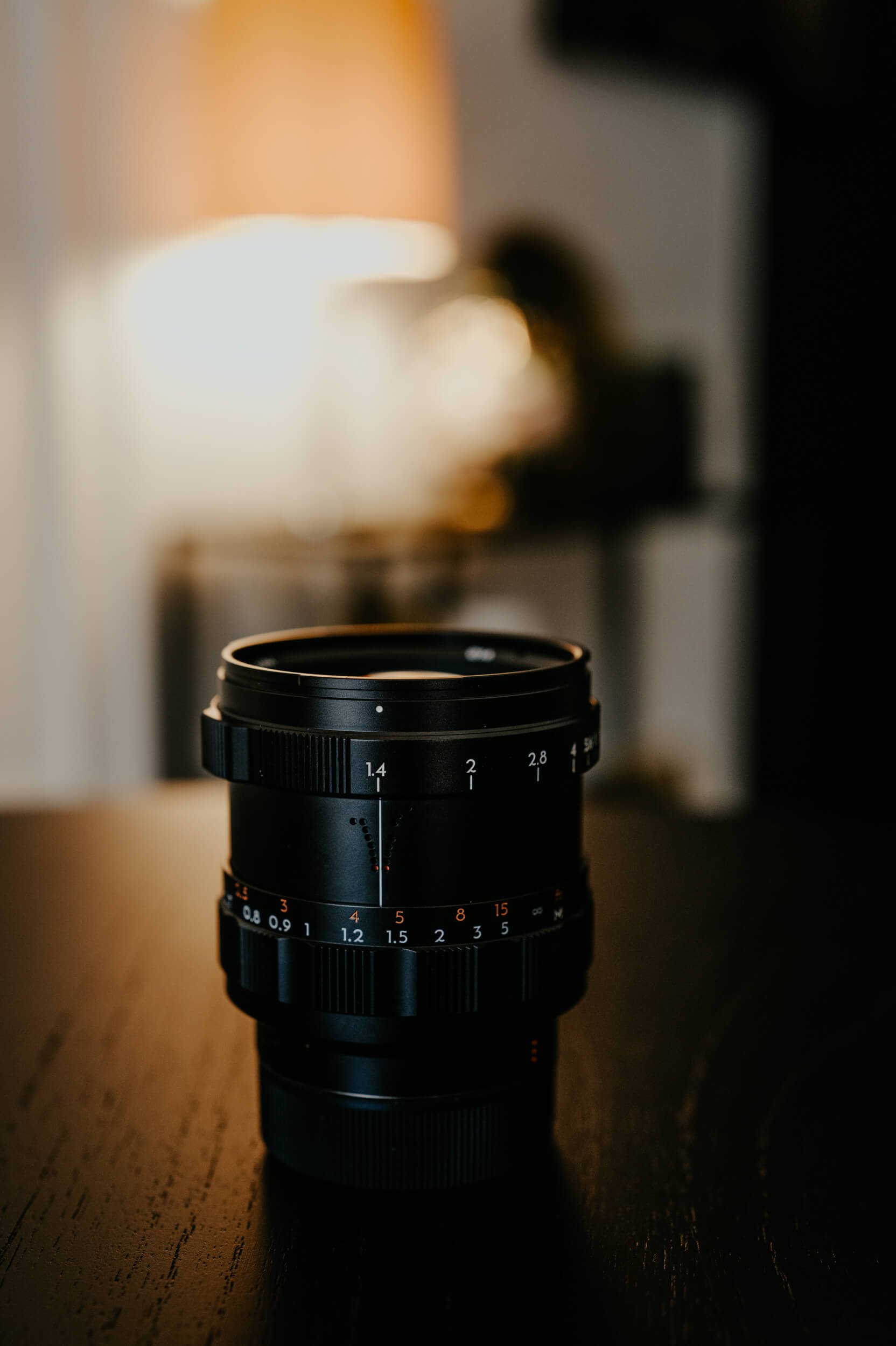 Thypoch Simera 75mm f/1.4 M-mount lens photographed upright on a wooden table in warm, cinematic light.