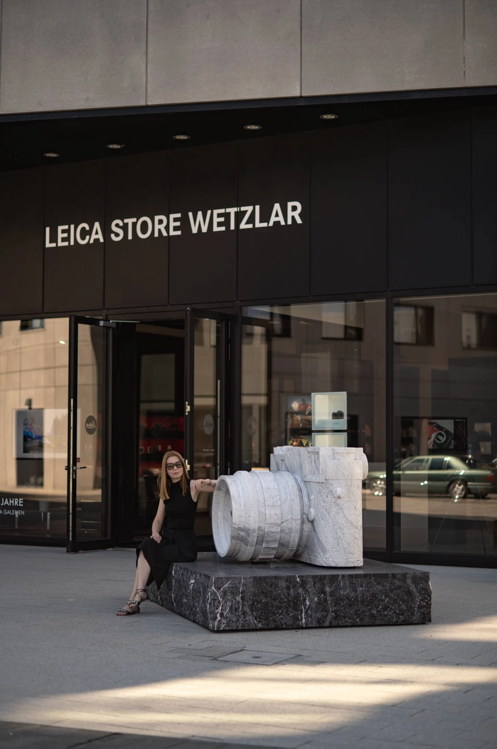 Aliya sitting beside the Carrara marble Leica sculpture outside Leica Store Wetzlar, photographed with the Leitz Summicron-M 66 f/2.