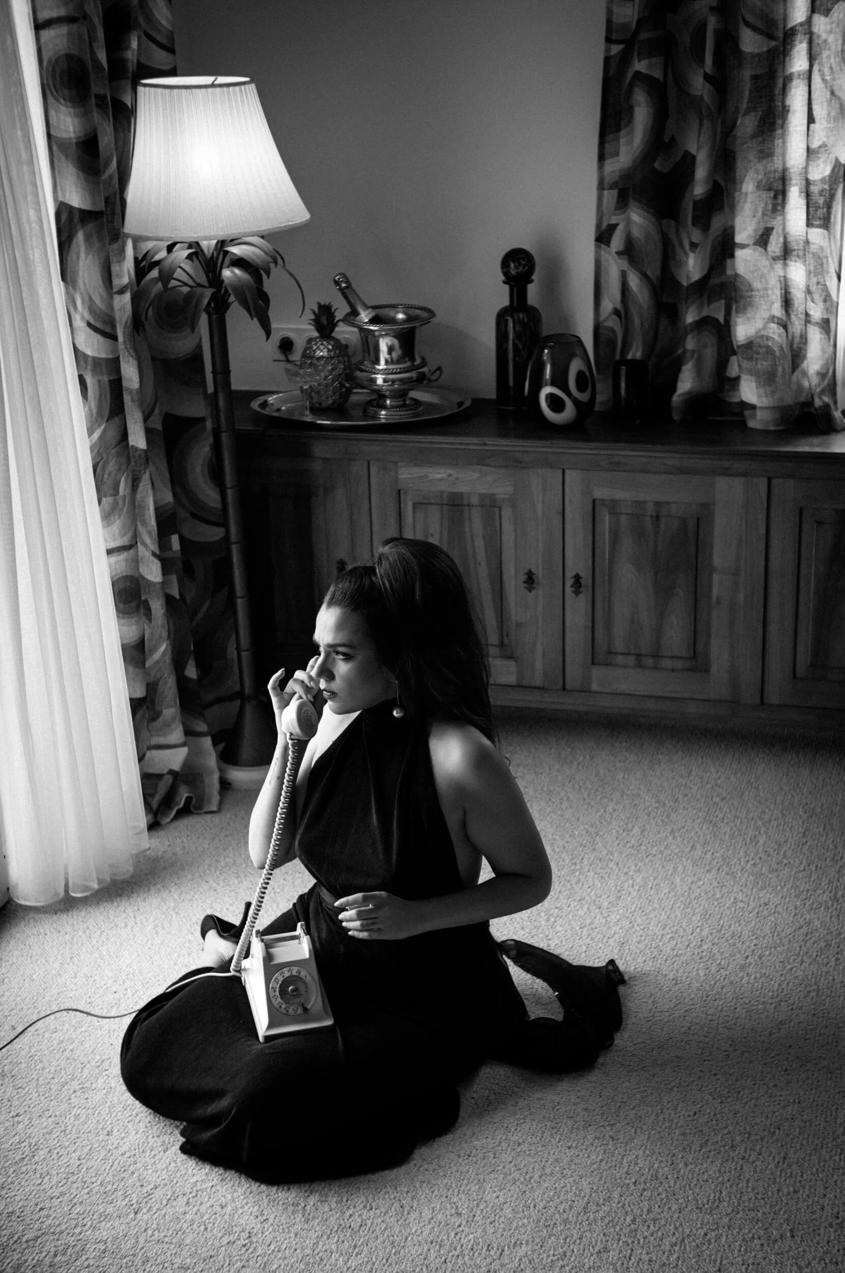 Black and white portrait of a woman sitting on the floor speaking on a vintage telephone photographed with the Omnar Bertele 50mm f/2