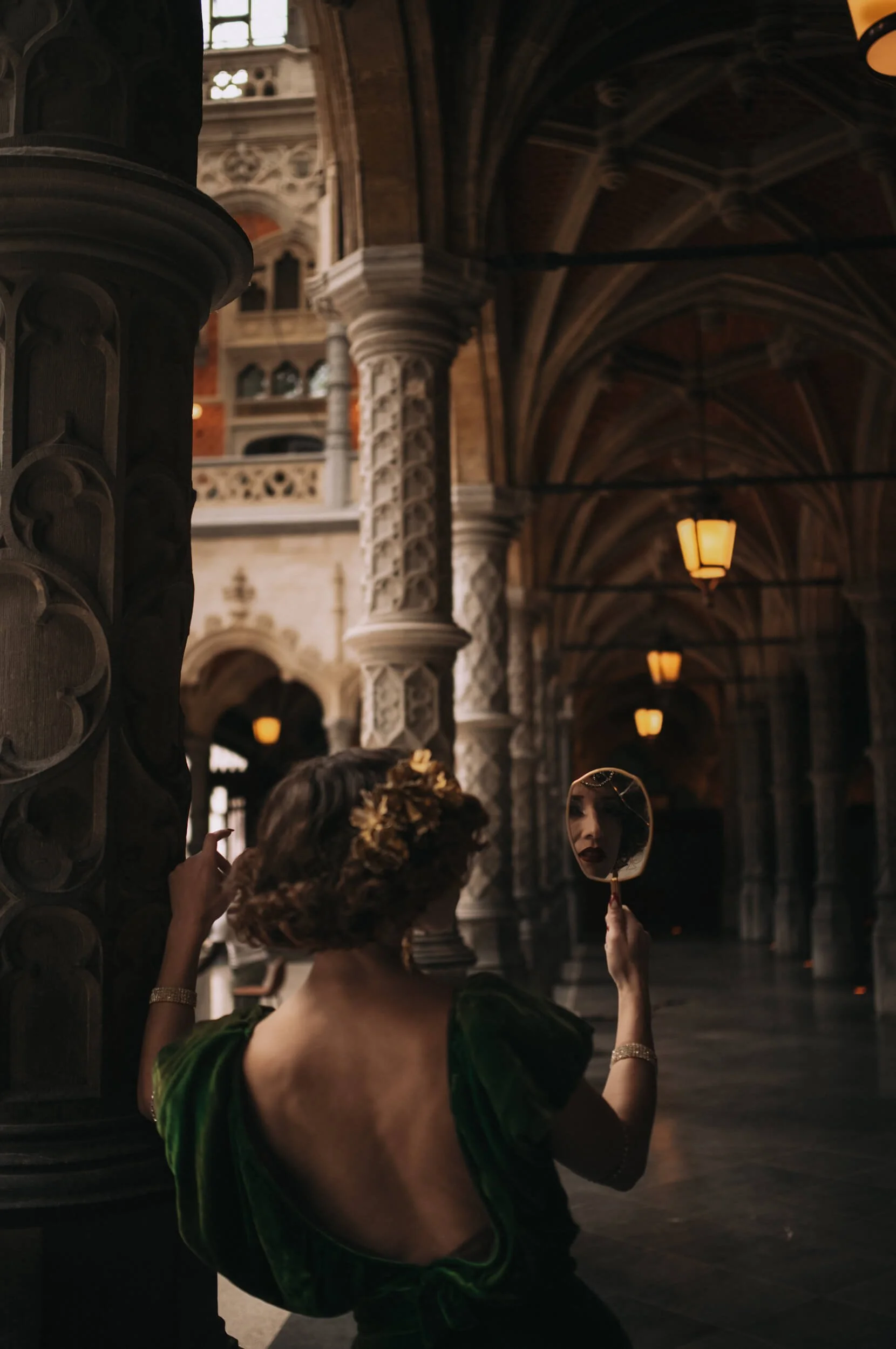 Chanelle holding a vintage mirror beneath the Gothic arcades of the Handelsbeurs in Antwerp, with her reflection framed by warm architectural light, photographed with the Thypoch Simera 35mm f/2.