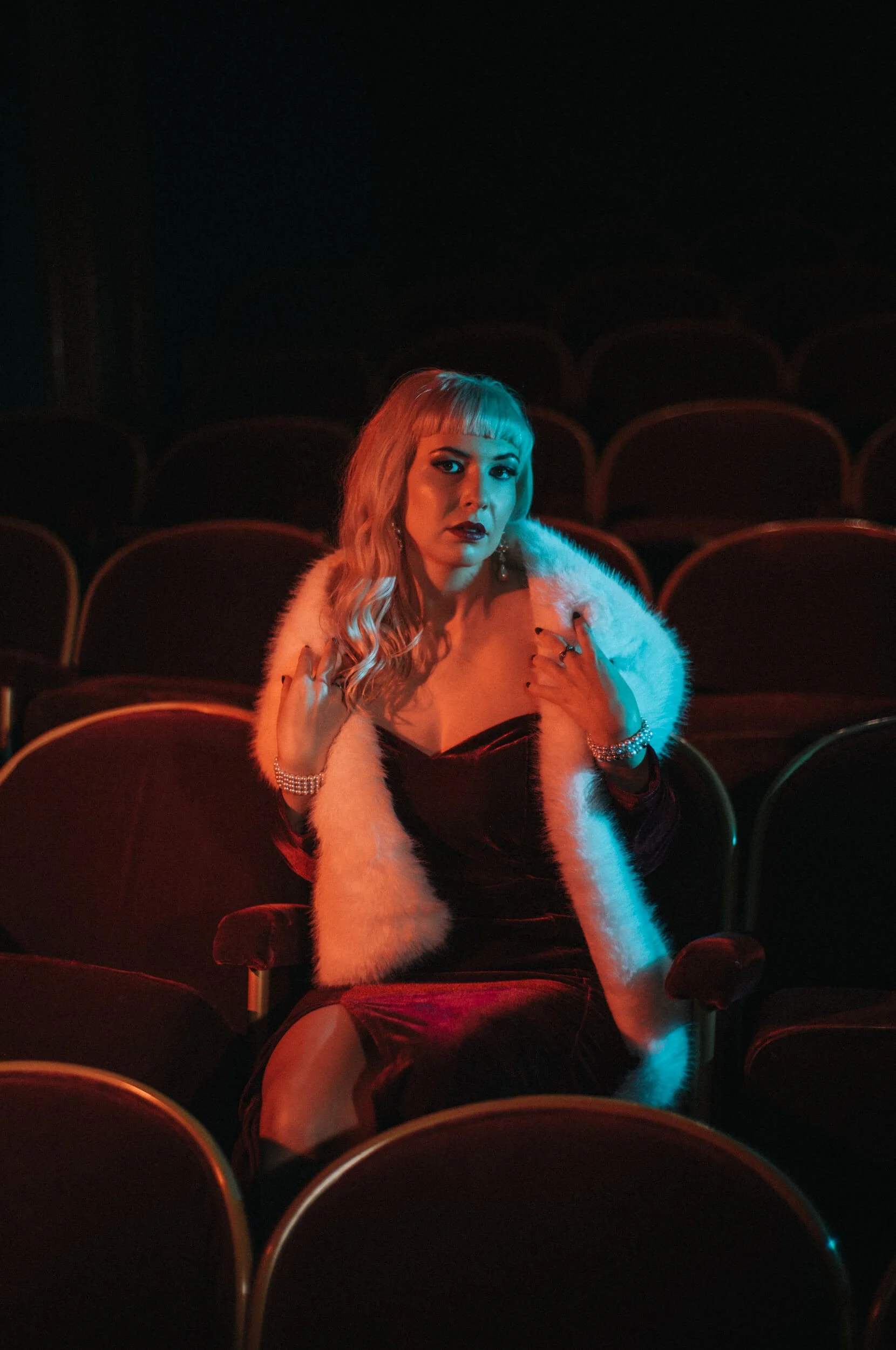 Cinematic portrait of Laura in a red velvet cinema seat, photographed with the Mandler 50mm f/1.4 E46 Pre-A lens on the Leica M11-D using red and cyan lighting.