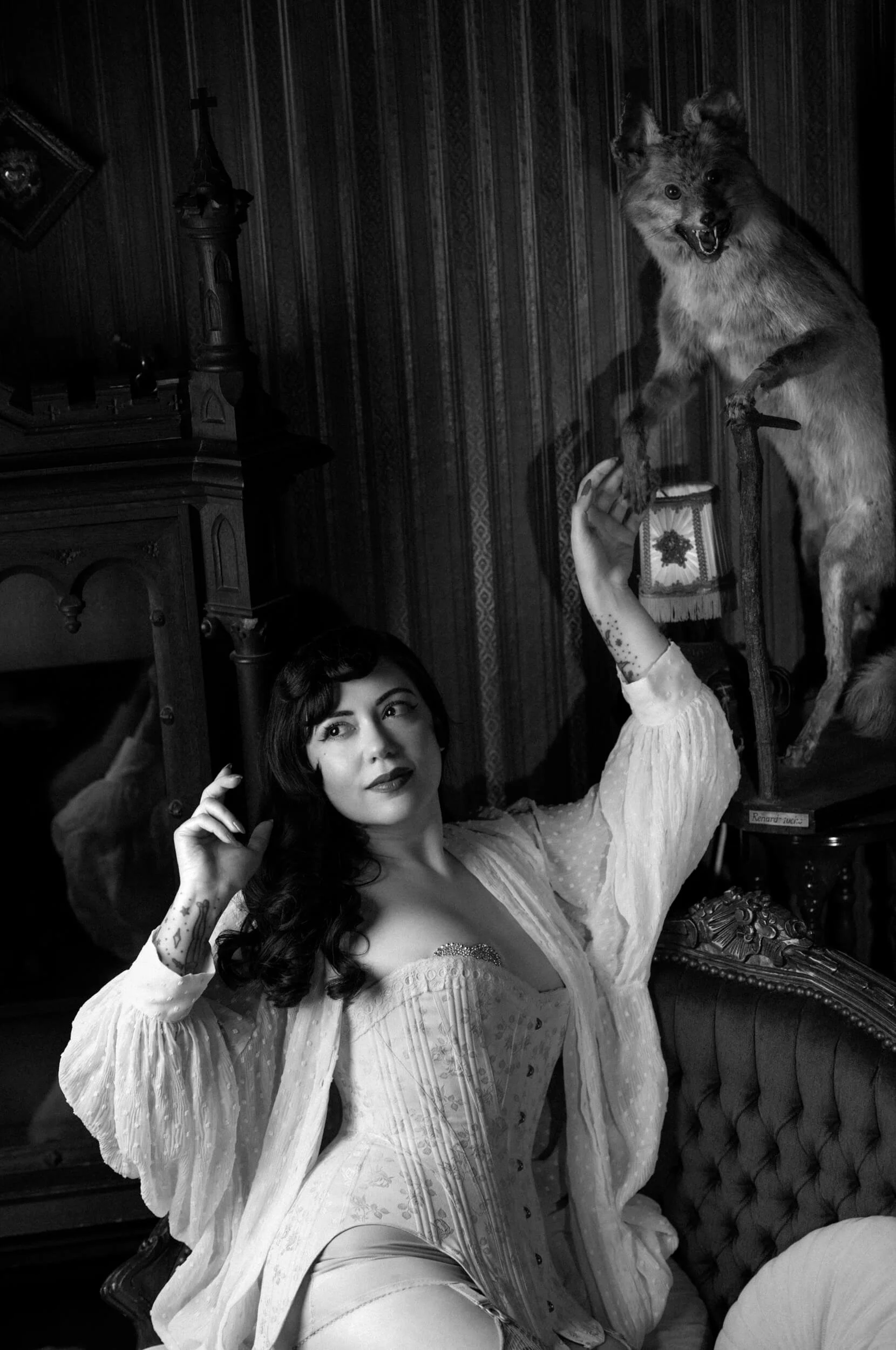 Black-and-white portrait of Bettie From Hell beside a fox taxidermy, photographed with the Thypoch Simera 75mm f/1.4 on the Leica M11 Monochrom.
