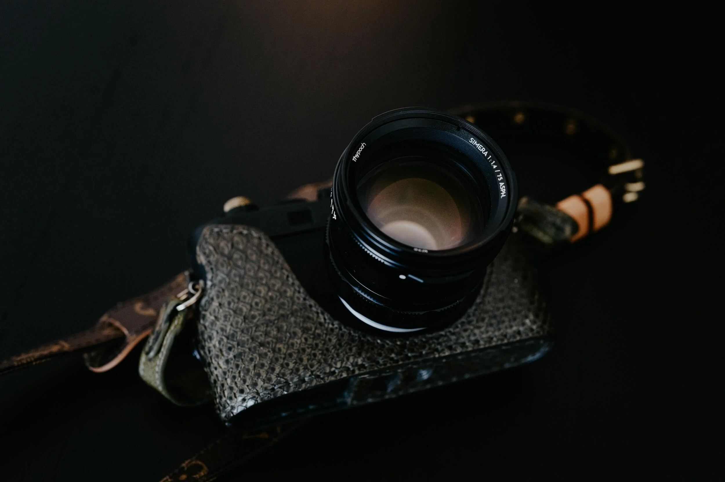 Thypoch Simera 75mm f/1.4 M-mount lens resting on a Leica M camera with a textured leather case and camera strap.