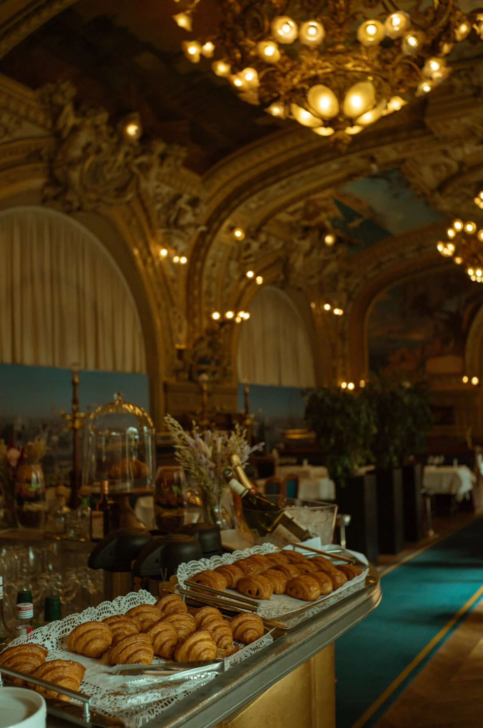 Fresh croissants displayed at breakfast inside Le Train Bleu at Gare de Lyon in Paris, with the restaurant's ornate chandeliers and Belle Époque interior in the background.