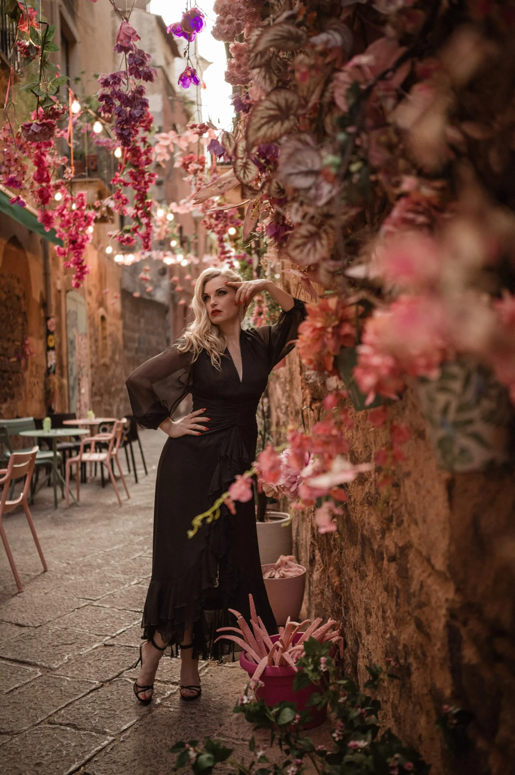 Roberta photographed wide open at f/2 in a flower-filled Sicilian alleyway, demonstrating the Thypoch Ksana 35mm f/2's layered rendering and environmental storytelling