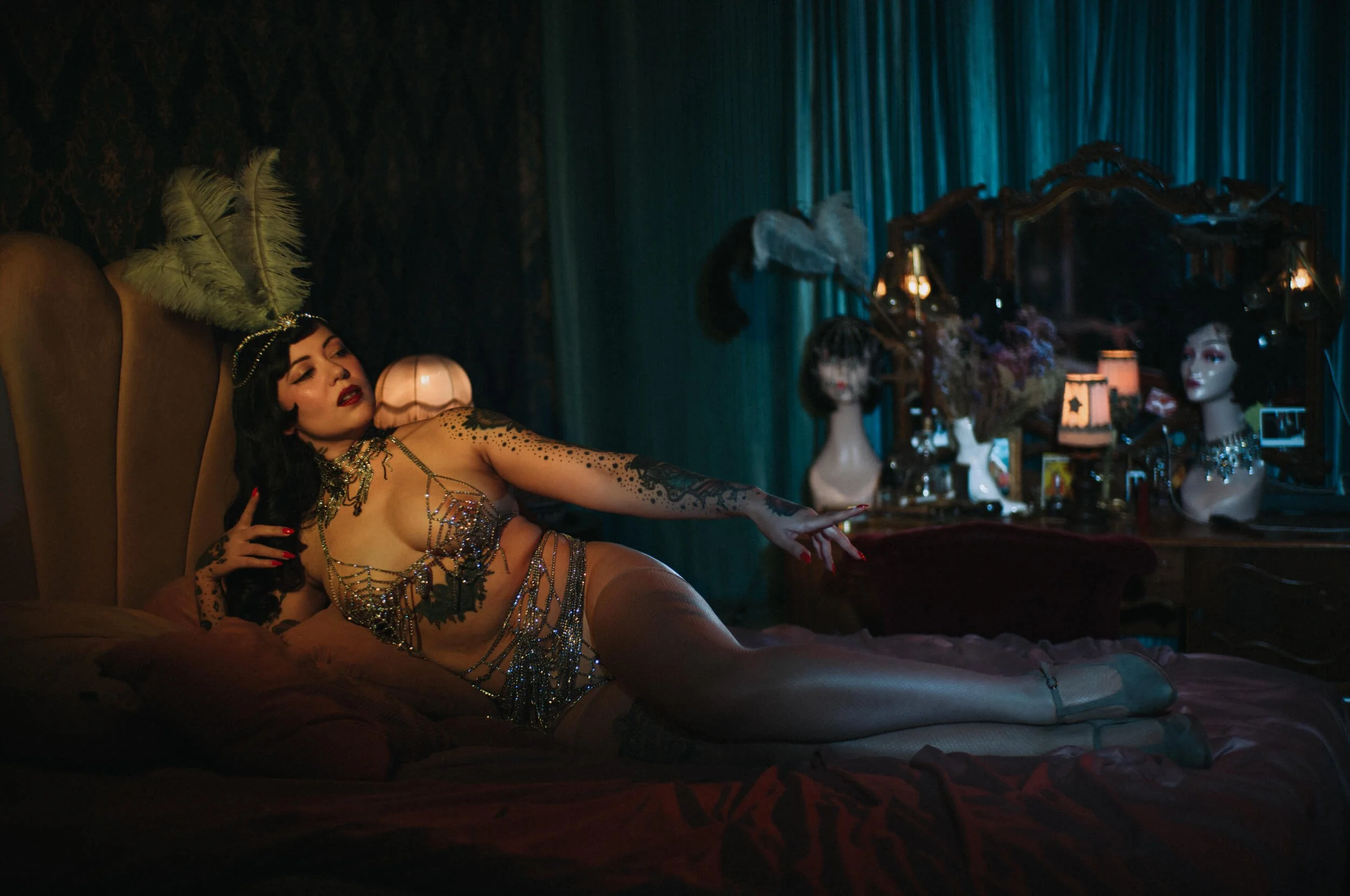 Horizontal cinematic portrait of Bettie from Hell reclining on a bed, photographed with the Mandler 50mm f/1.4 E46 Pre-A using warm and teal lighting.