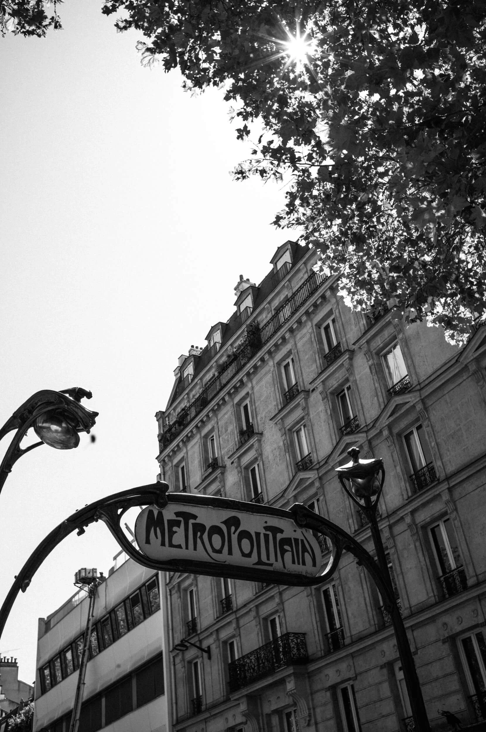 Black and white photograph of a Paris Métropolitain sign beneath a Haussmann building, shot with the Leica M11 Monochrom and Mandler 35mm f/2 lens.