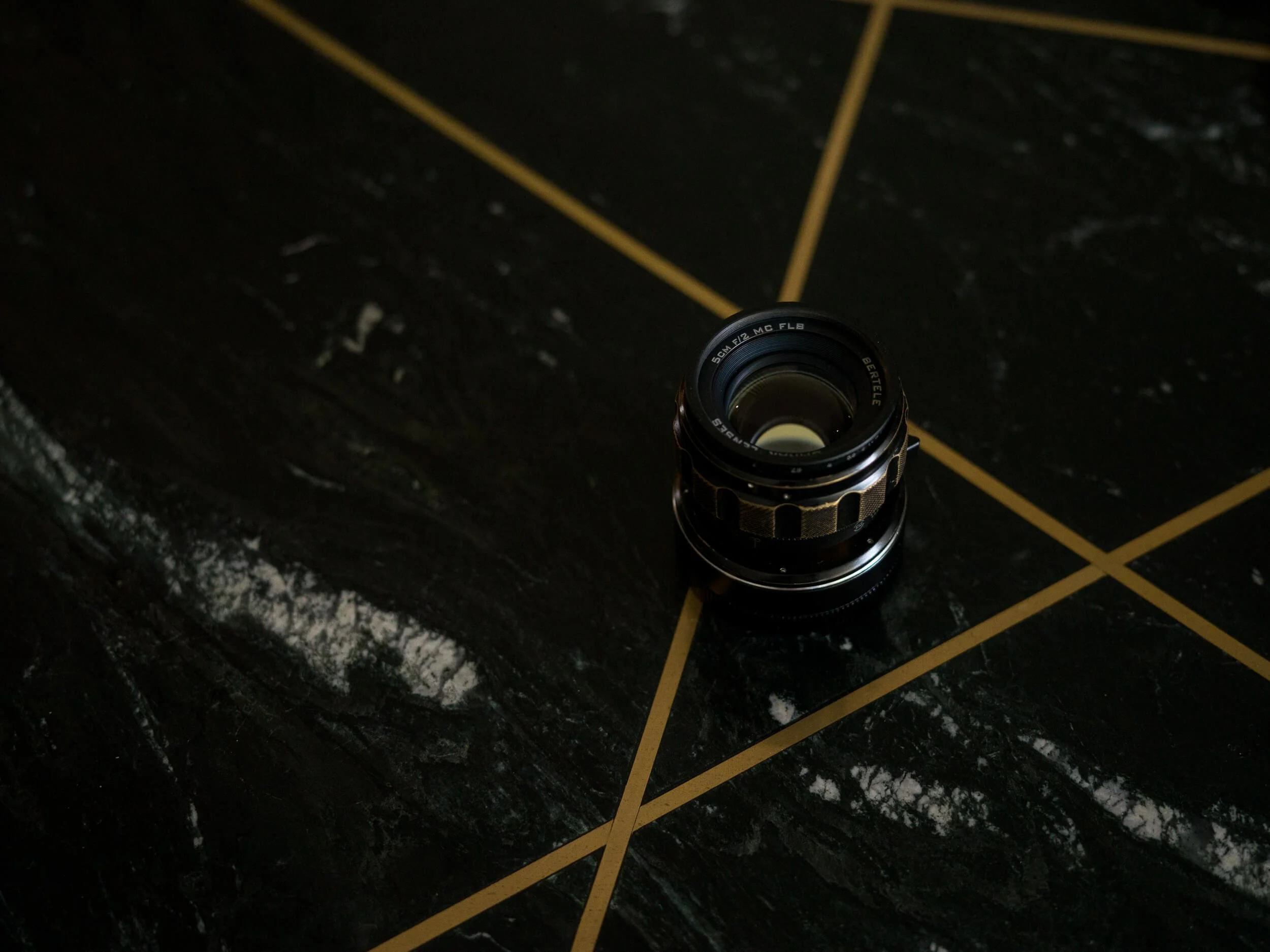 Omnar Bertele 50mm f/2 MC FLB lens photographed on a dark marble table with gold geometric lines
