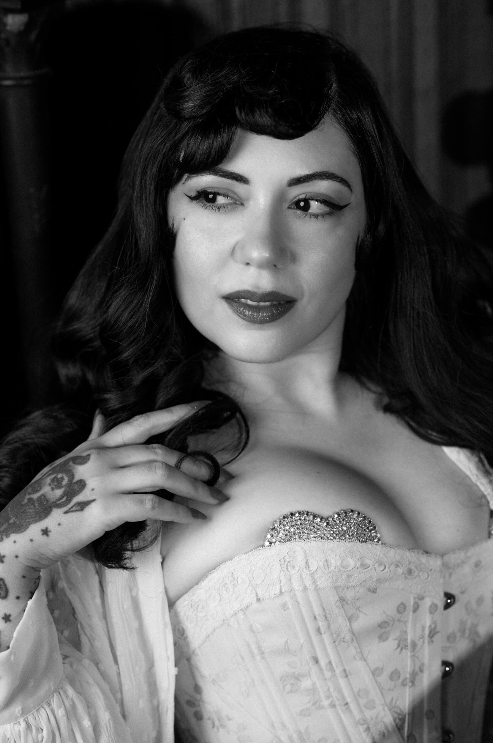 Black-and-white portrait of Bettie From Hell in a white corset, photographed with the Thypoch Simera 75mm f/1.4 on the Leica M11 Monochrom by Milan Swolfs.