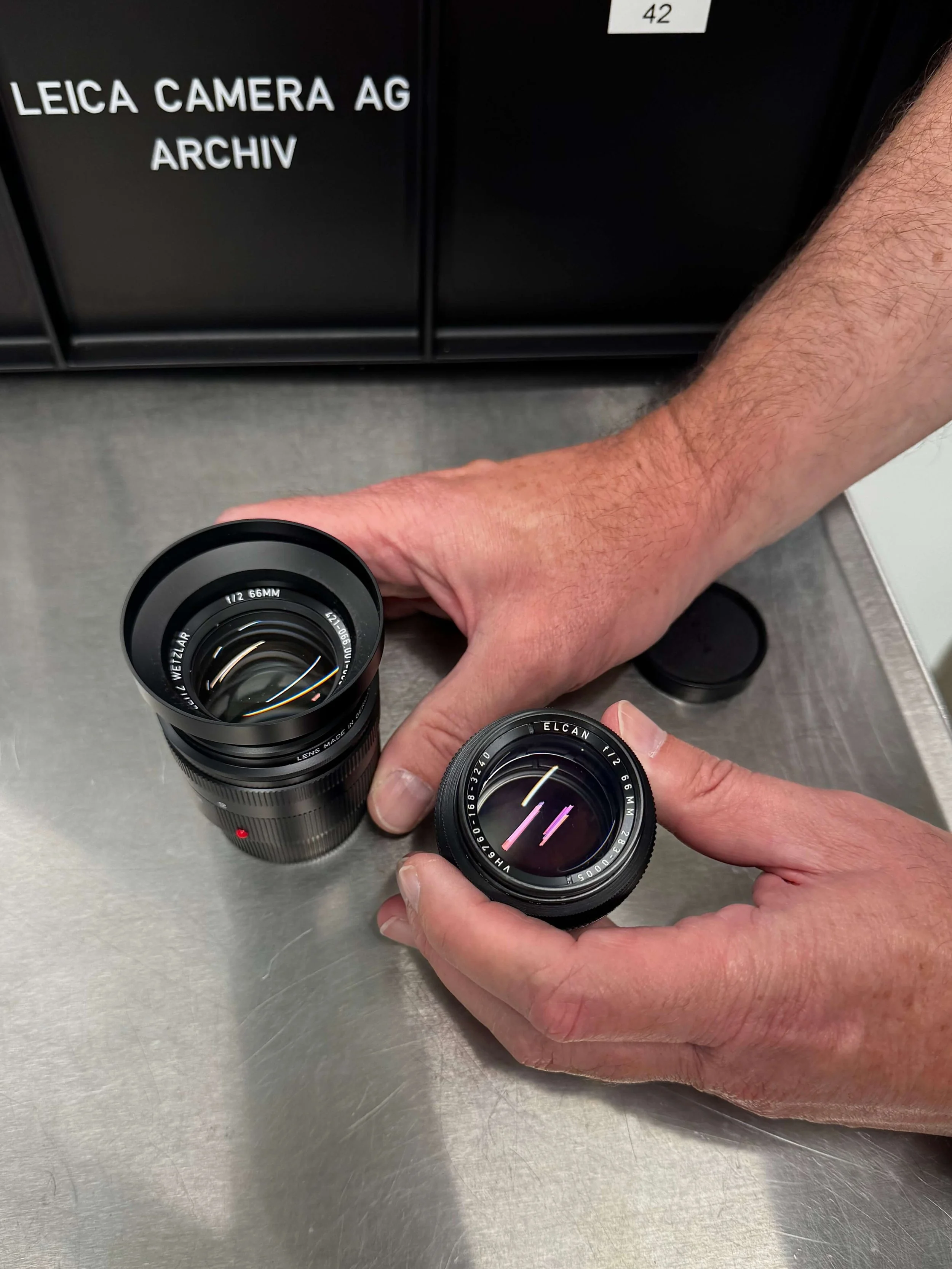 Tim Pullmann holding the Leitz Summicron-M 66 f/2 and the original ELCAN 66mm f/2 in the Leica Archives, photographed with an iPhone 15 Pro.