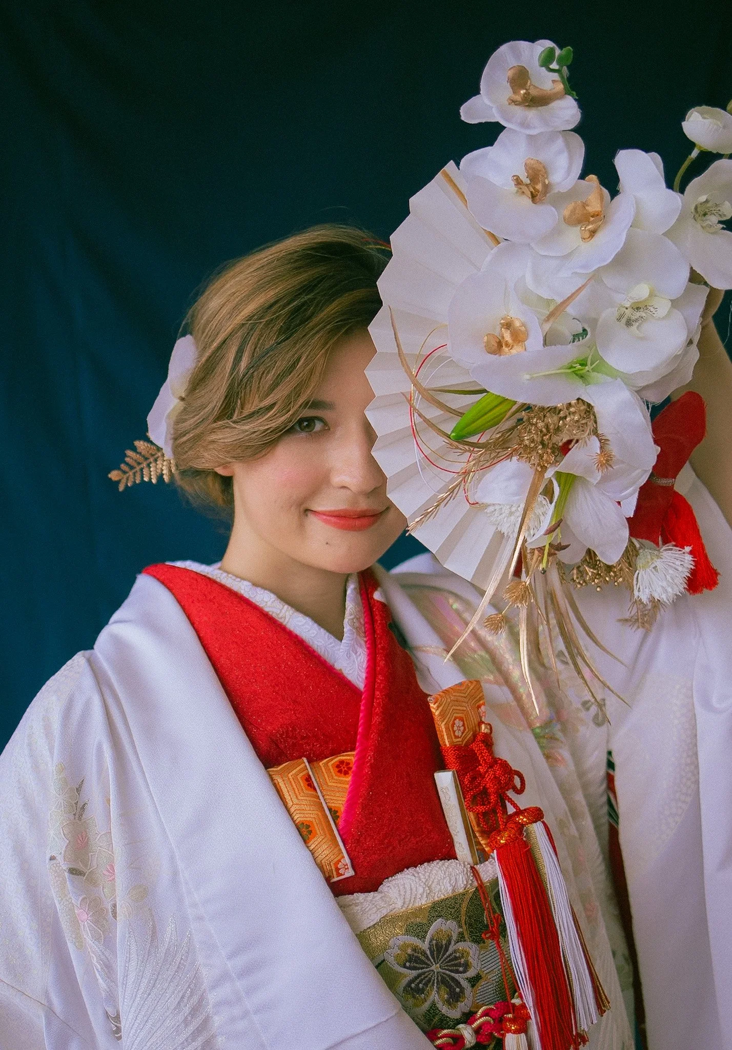 A young woman dressed in a traditional Japanese kimono, holding a bouquet of white orchids and a paper fan, smiling softly.