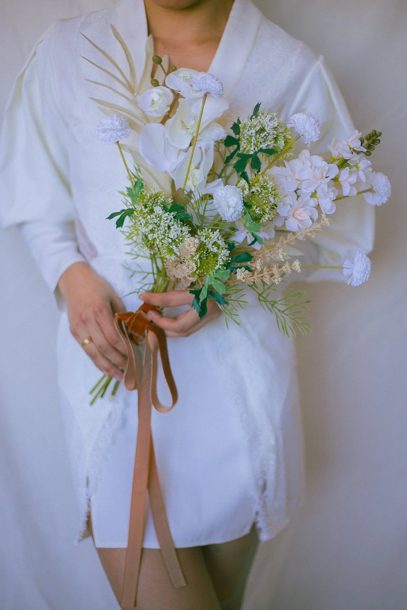 Person in white robe holding a bouquet of white flowers with a brown ribbon.