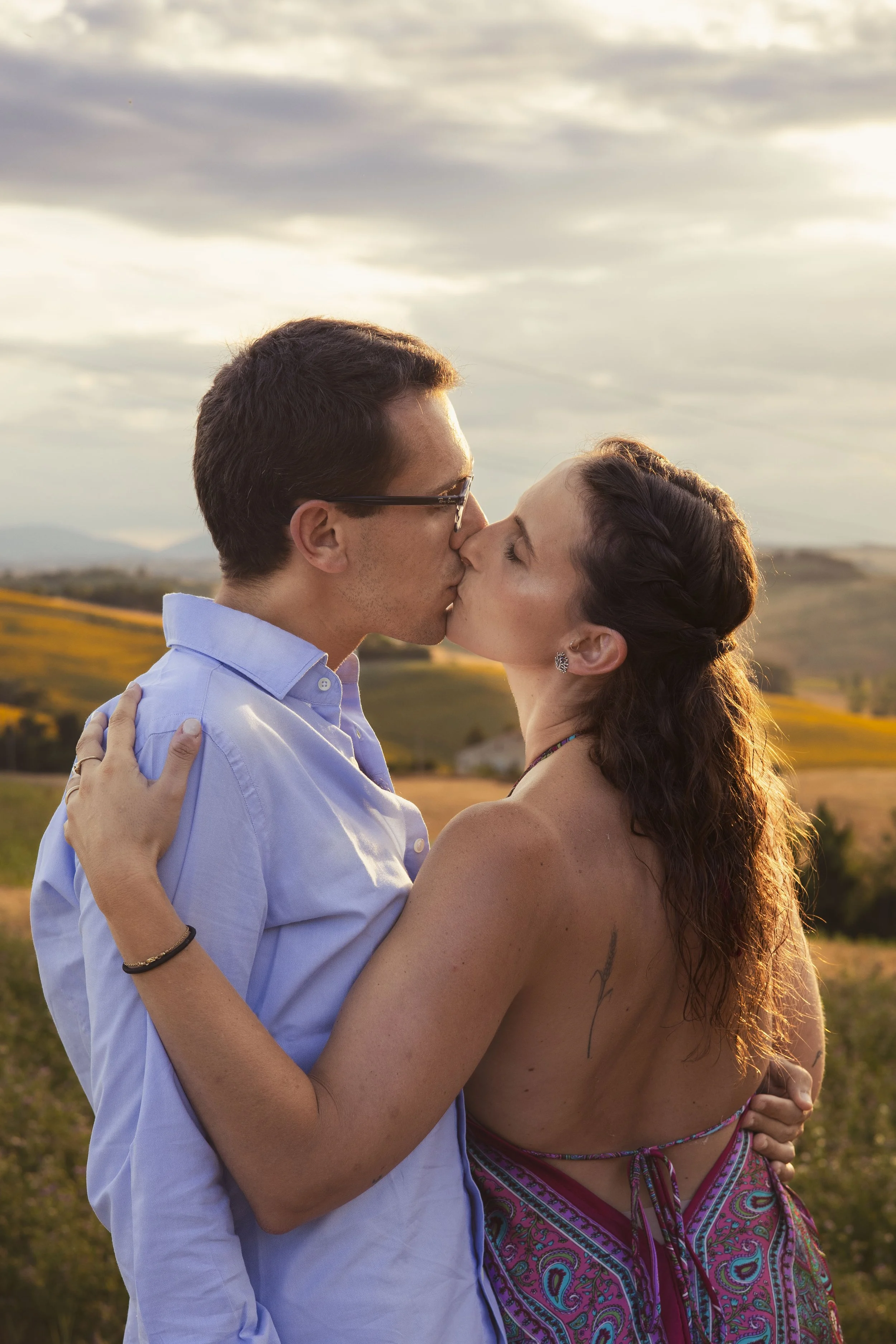 Una coppia si bacia in un campo durante il tramonto.