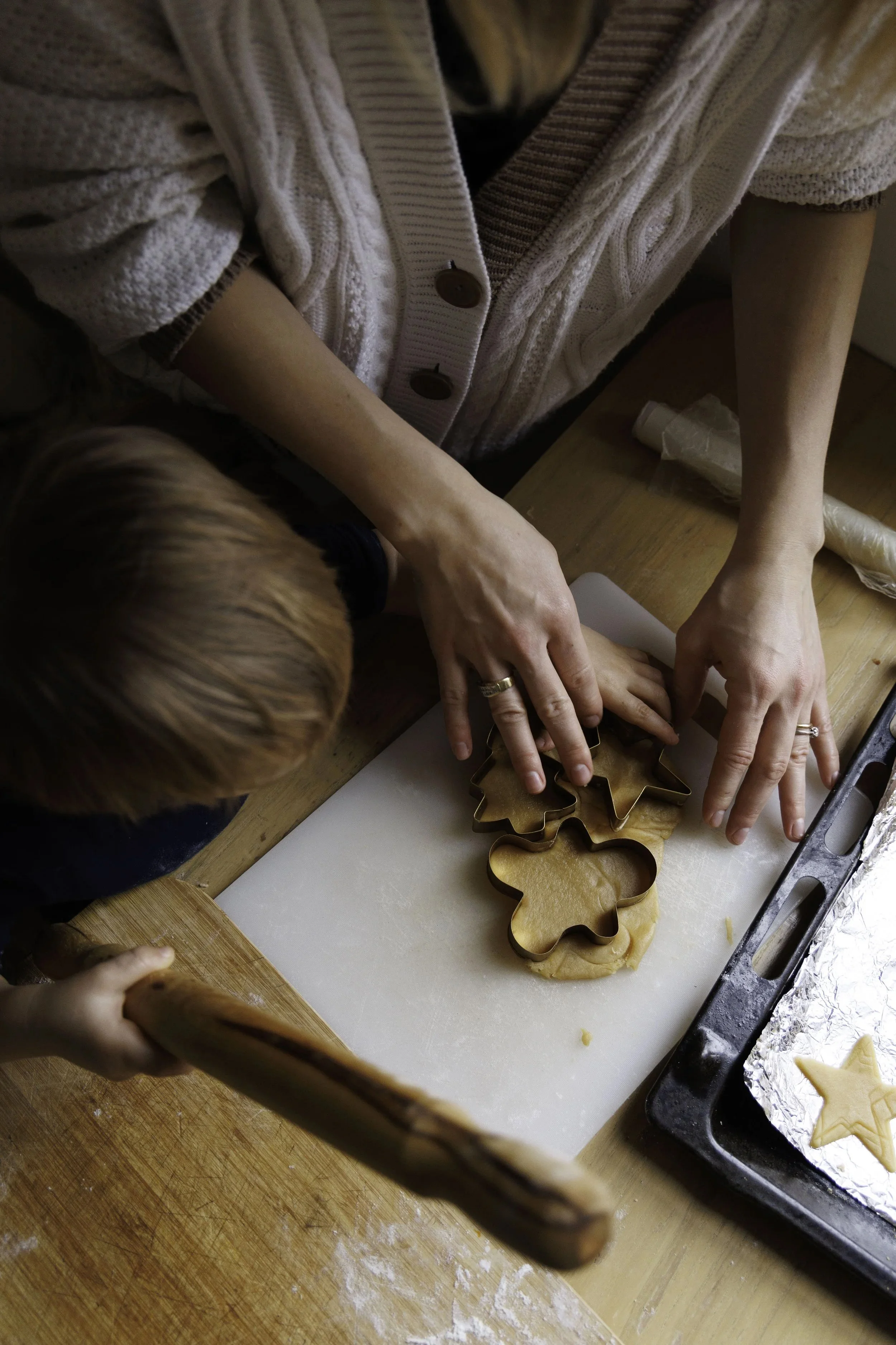 Una persona adulta e un bambino stanno tagliando biscotti di pasta frolla con delle formine in metallo su un piano di lavoro.