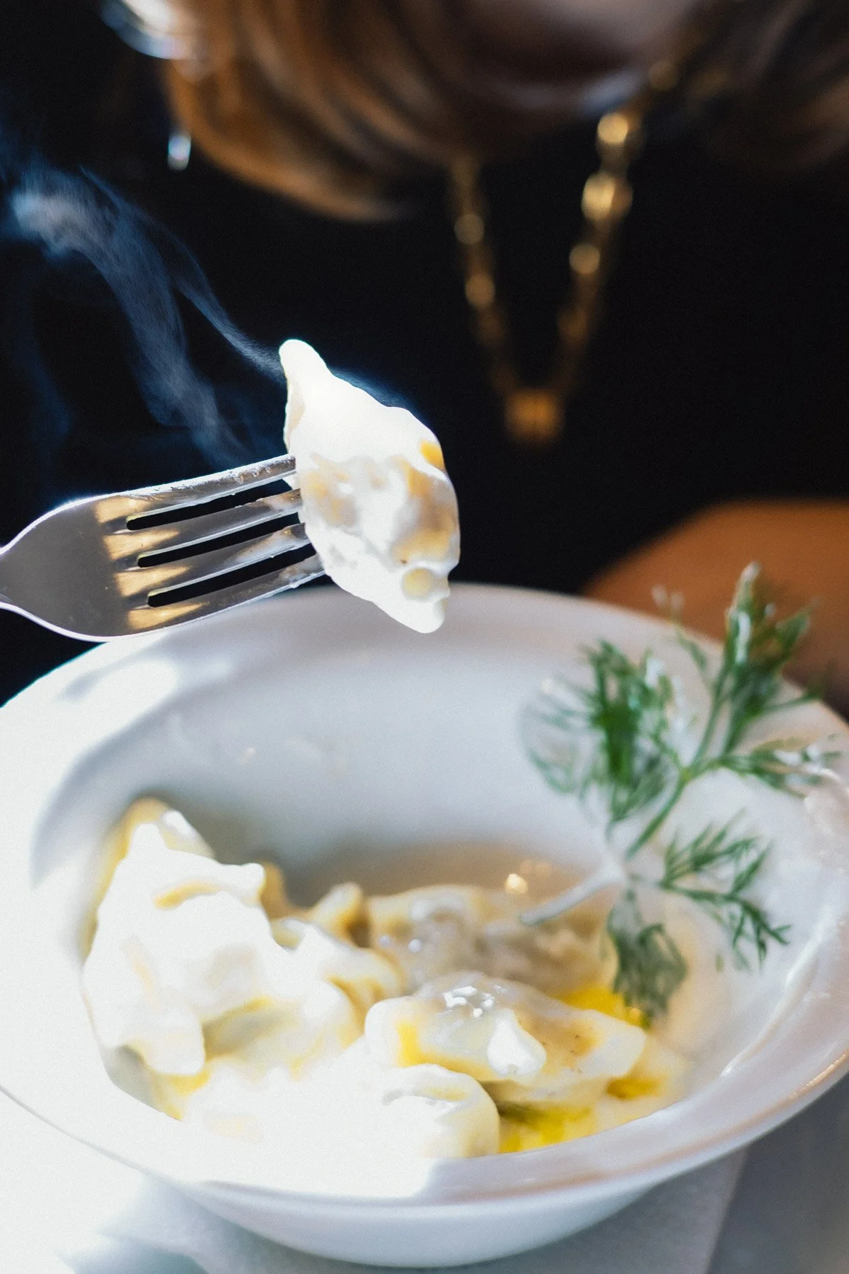 Piatti di pasta con salsa cremosa, decorati con erba fresca. Un cucchiaio con pasta è tenuto sopra una ciotola bianca.