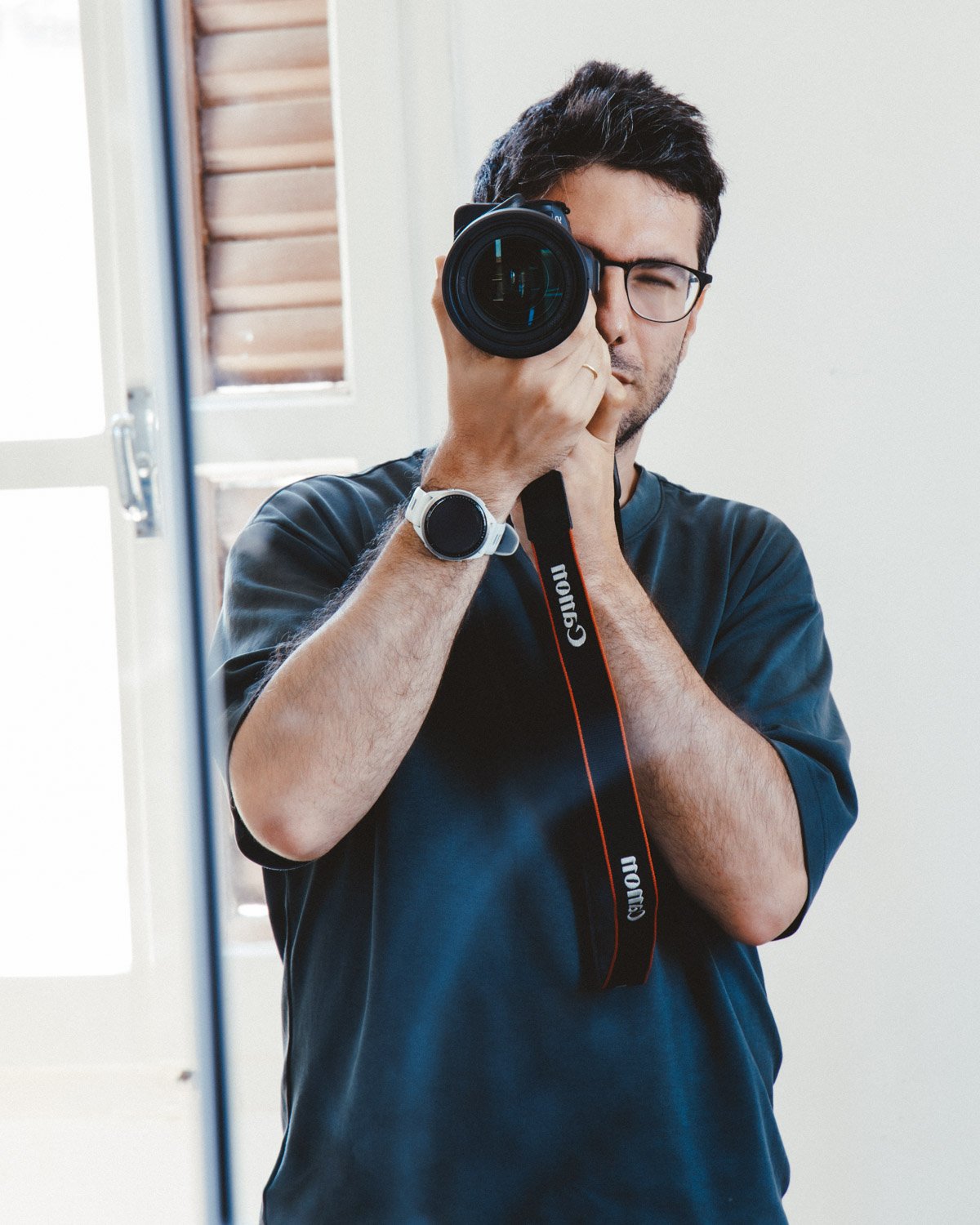 Uomo con occhiali neri che si sta scattando una foto con una fotocamera reflex davanti a uno specchio