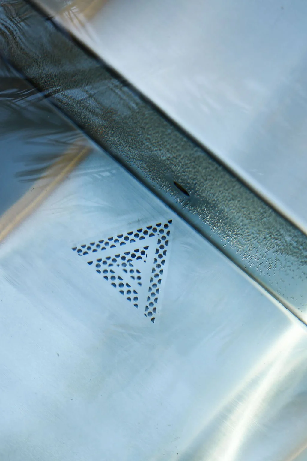 Close-up of a metallic surface with a perforated triangle pattern and a textured metal strip, reflecting light.