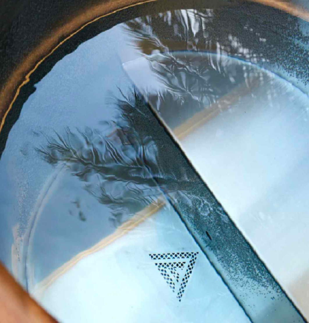 View through a car's side mirror reflecting trees and sky, with windshield showing the interior of the vehicle.