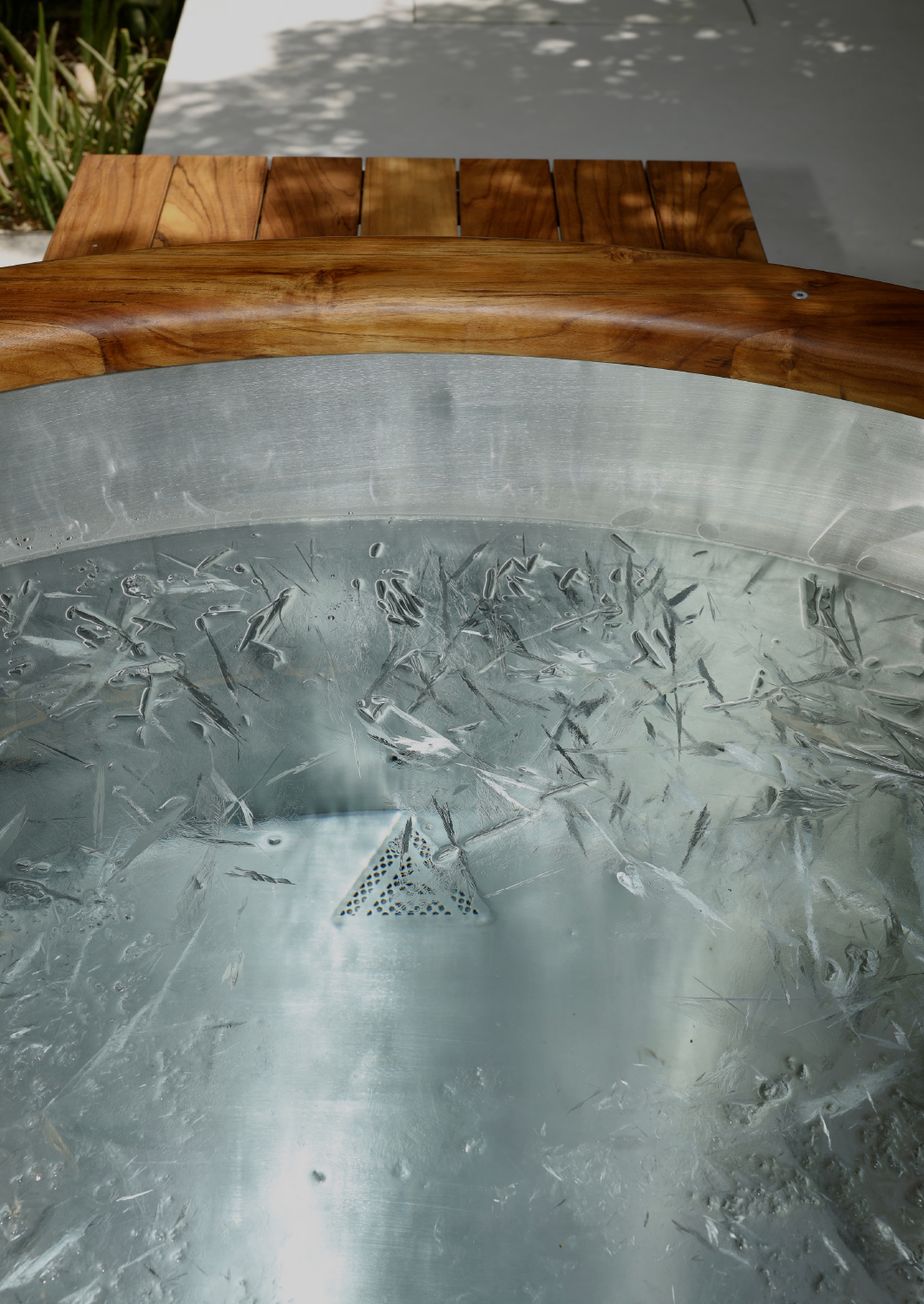Close-up of a circular ice table with a wooden rim and a metal lattice drain beneath the ice, outdoors with a blurred background.