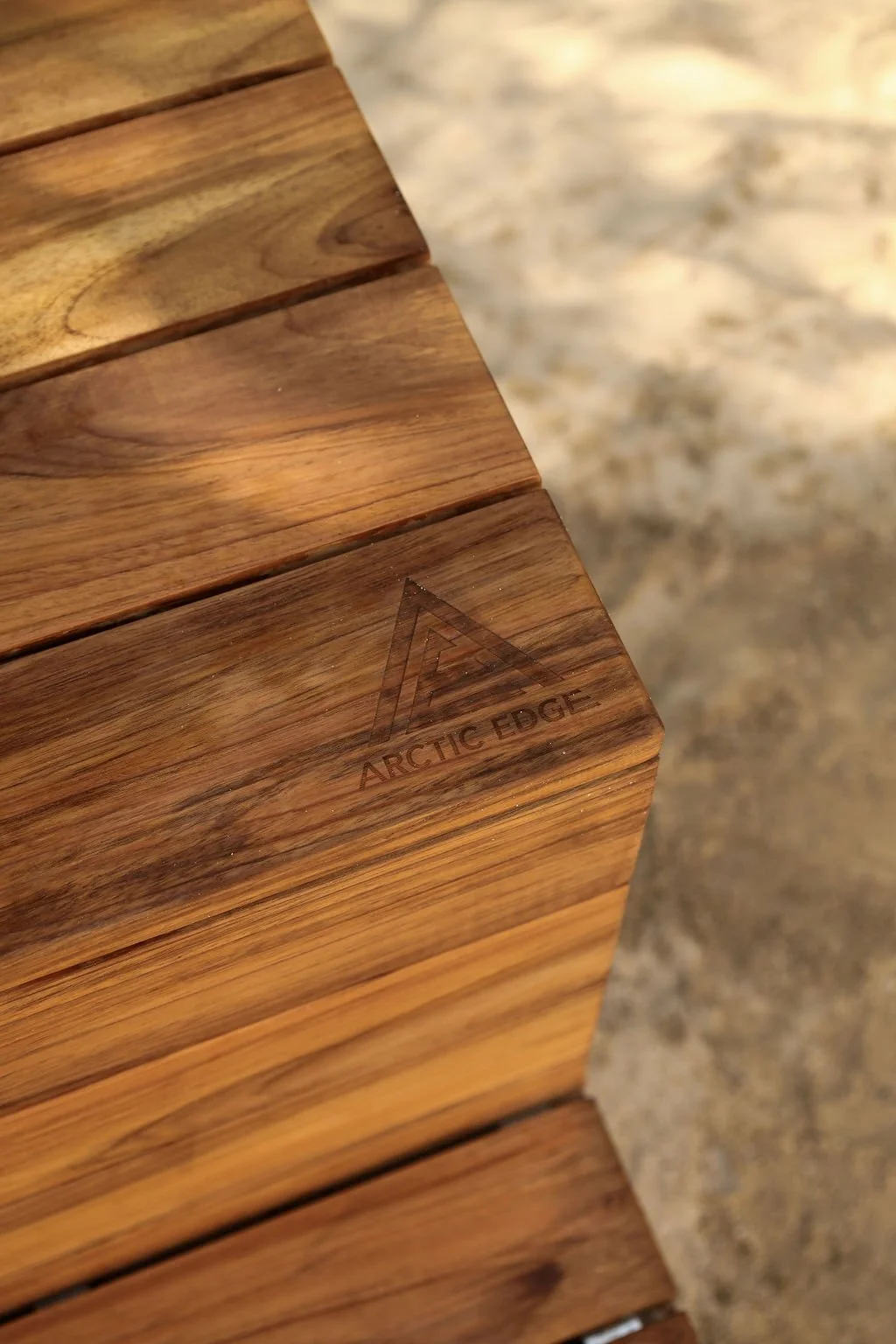 Close-up of a wooden surface with a logo that says 'Arctic Edge' and a mountain peak symbol, on a textured stone background.
