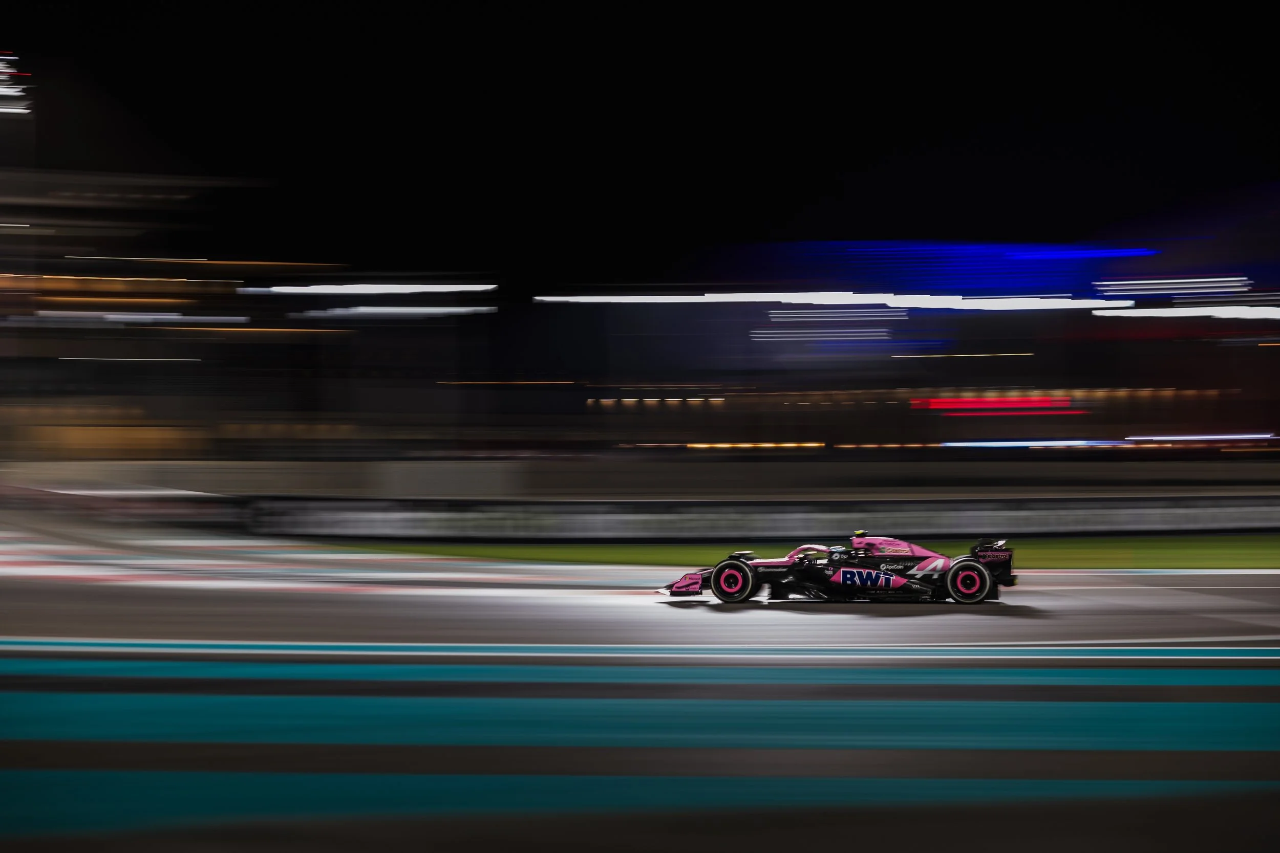 An Alpine F1 car whizzing past in focus against blurry lights.